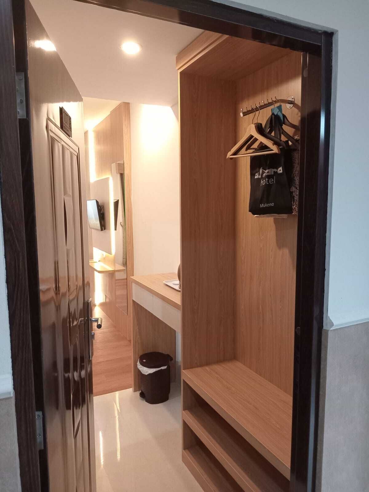 Ein Hotelzimmer mit einem Holzschrank, einer kleinen Sitzecke und einem Kleiderhaken, an dem eine schwarze Tasche hängt.