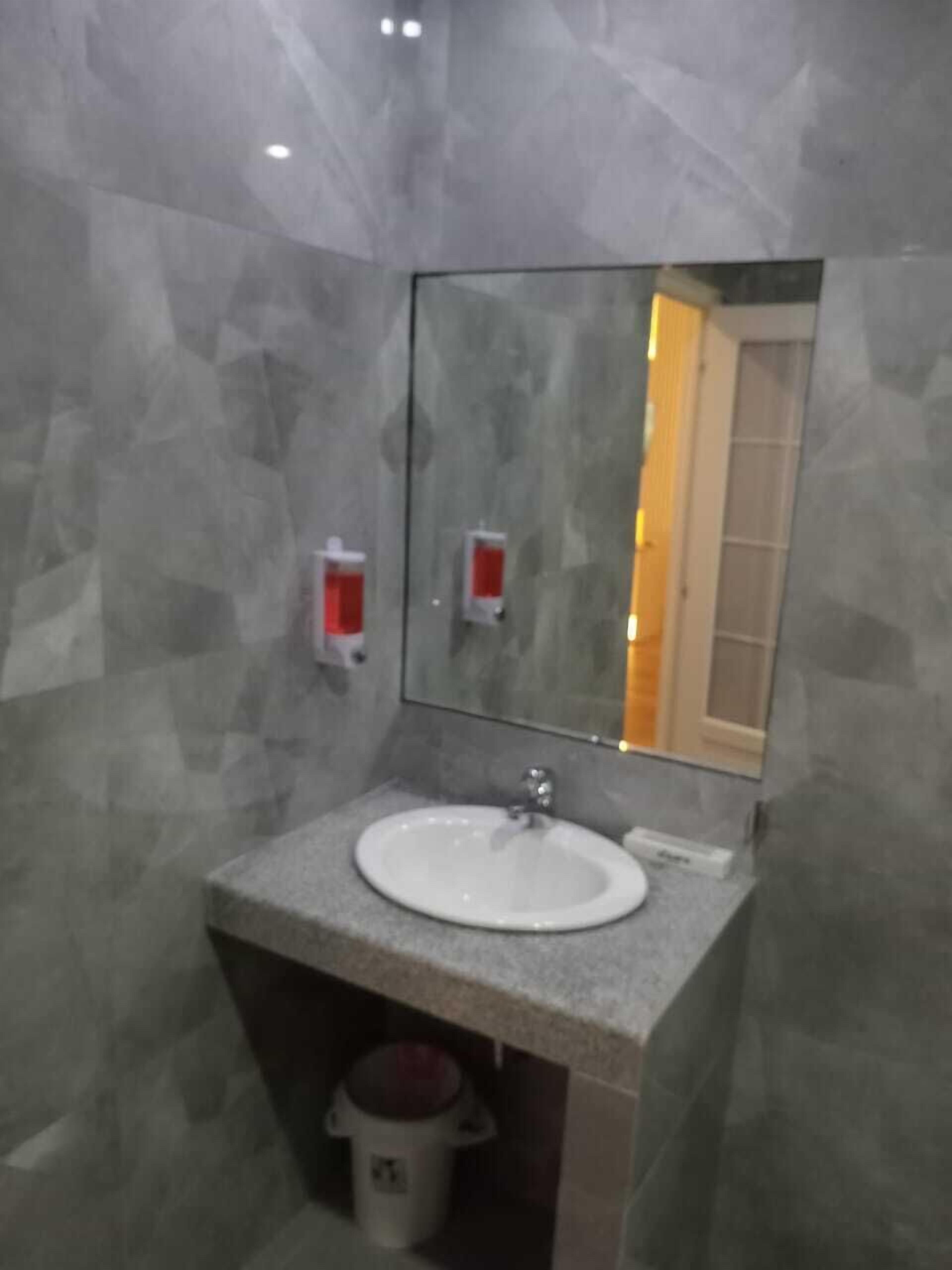 Ein Badezimmer mit Marmorwand, Waschbecken, Spiegel und Mülleimer.