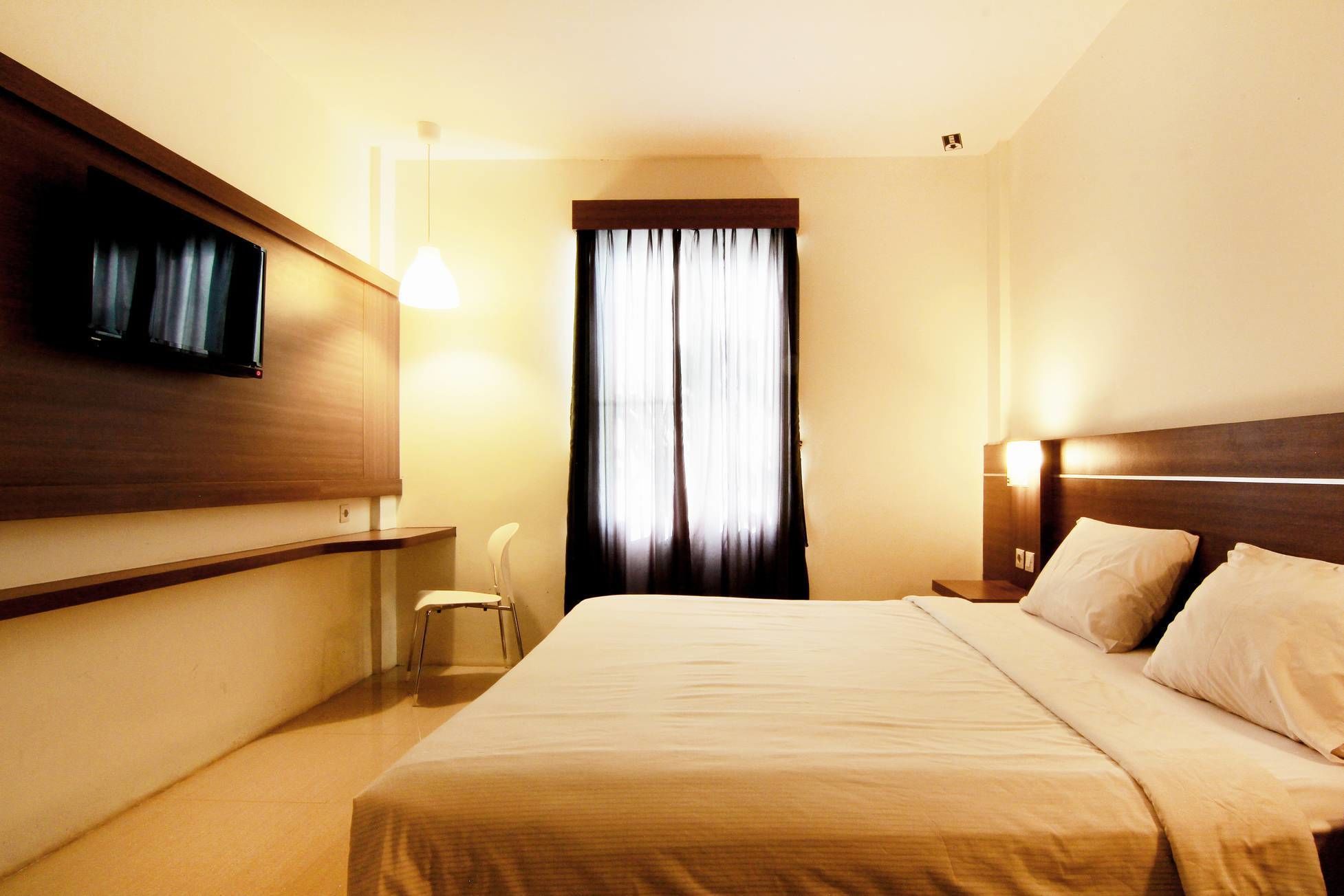 Una habitación de hotel con cama, mesitas de noche, televisor en la pared y ventana con cortinas.