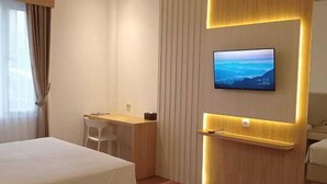 Una habitación de hotel con dos camas, un escritorio y un televisor montado en la pared.