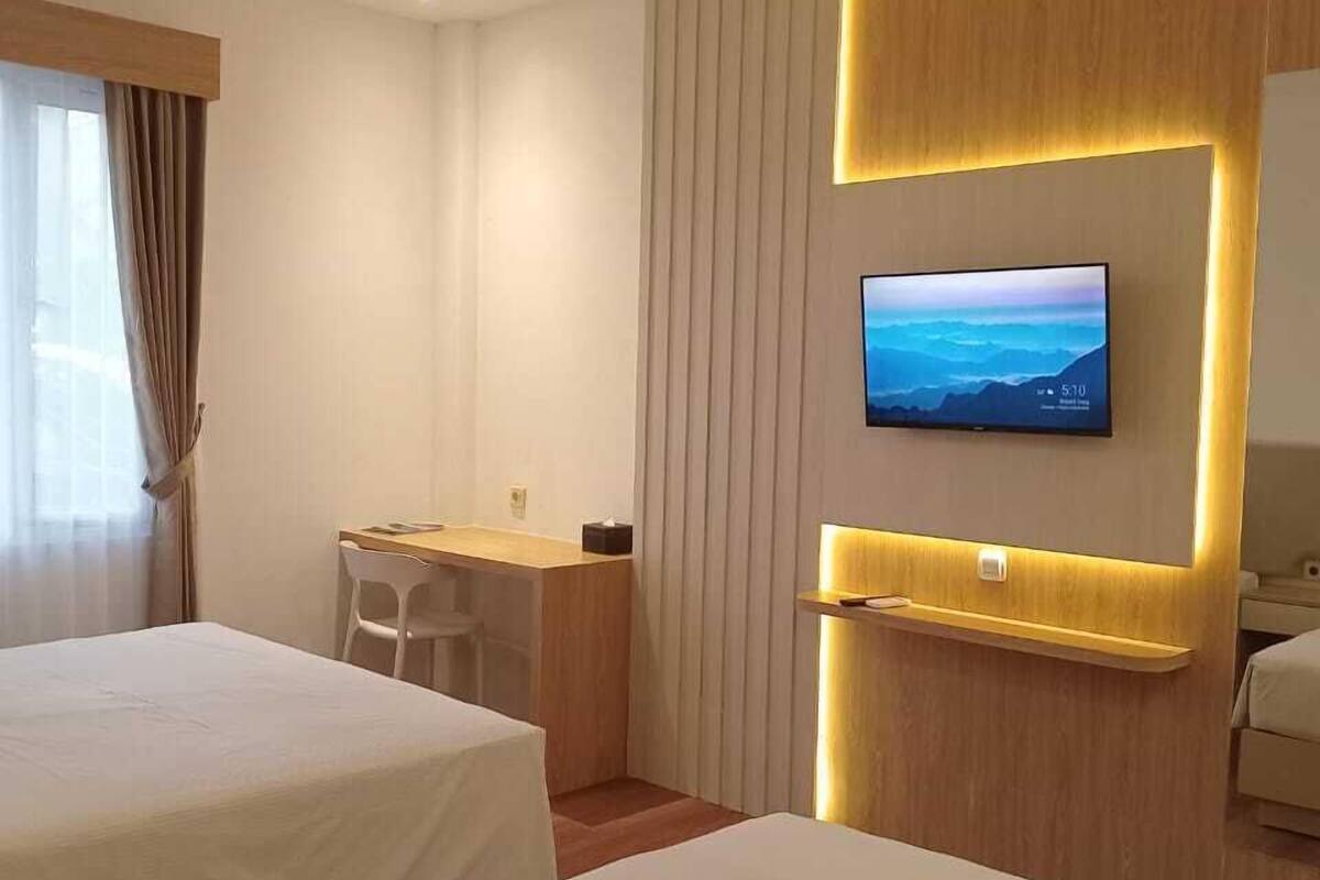 A hotel room with two beds, a desk, and a TV mounted on the wall.
