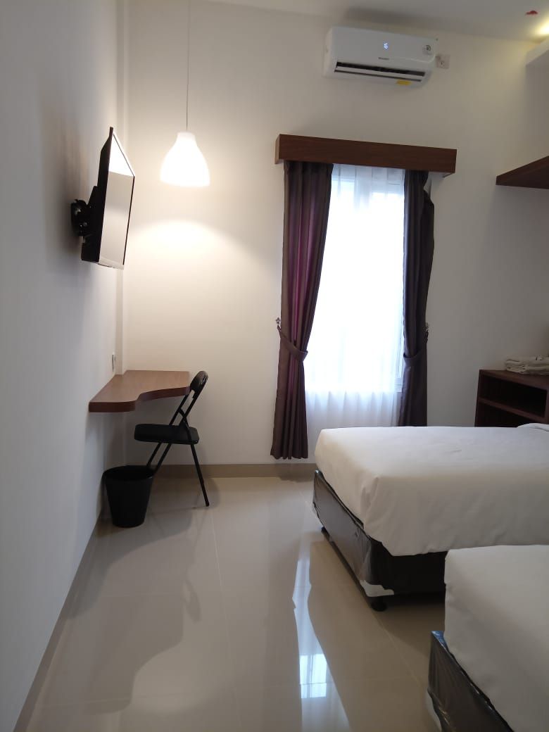 Ein Hotelzimmer mit Bett, Schreibtisch, Stuhl, Klimaanlage und einem fenster mit Vorhängen.