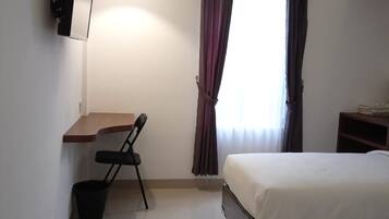 Ein Hotelzimmer mit Bett, Schreibtisch, Stuhl, Klimaanlage und einem fenster mit Vorhängen.