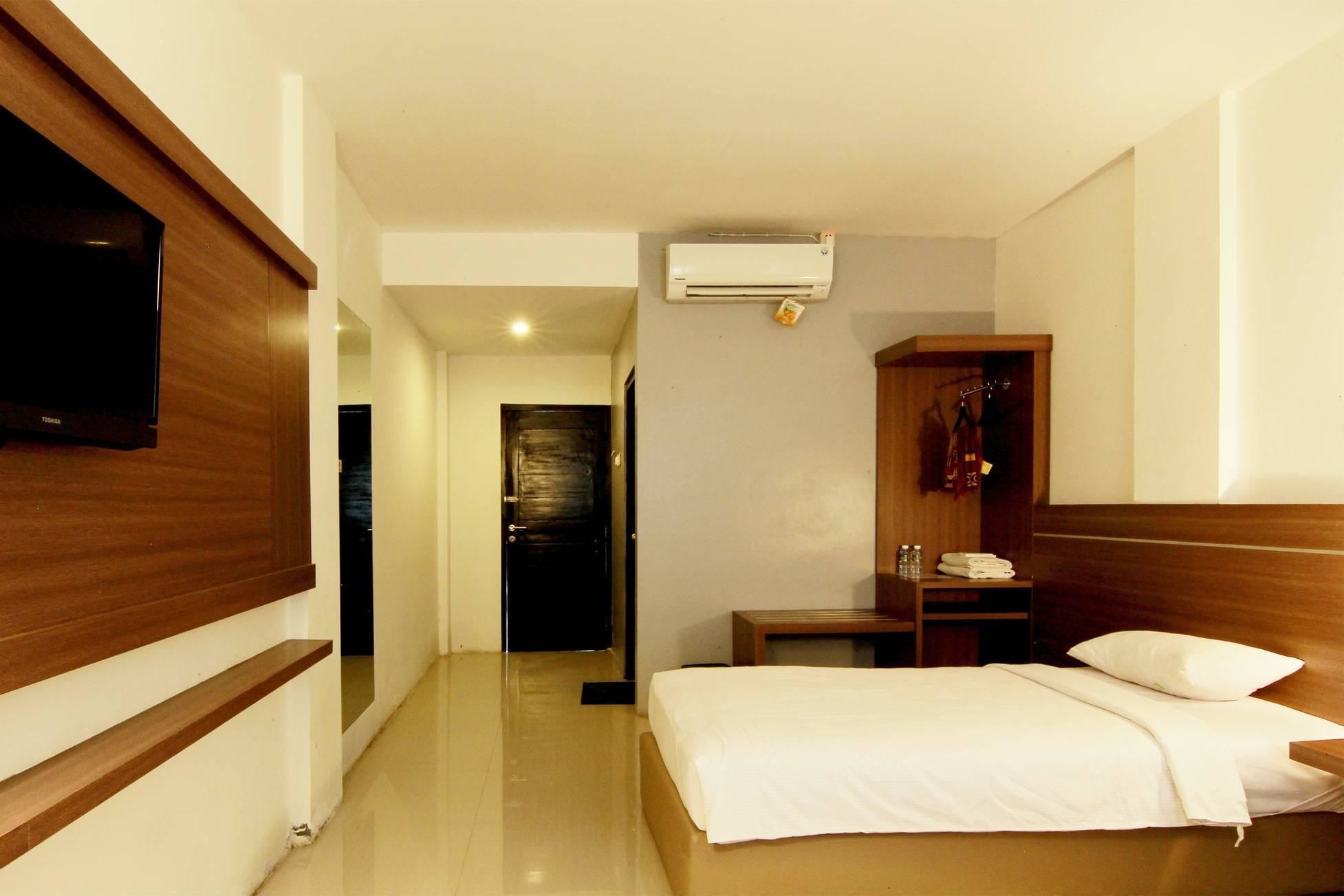 Une chambre d’hôtel avec un lit, un téléviseur fixé au mur, une armoire et une petite table sur laquelle se trouvent une bouteille et une boîte de mouchoirs.