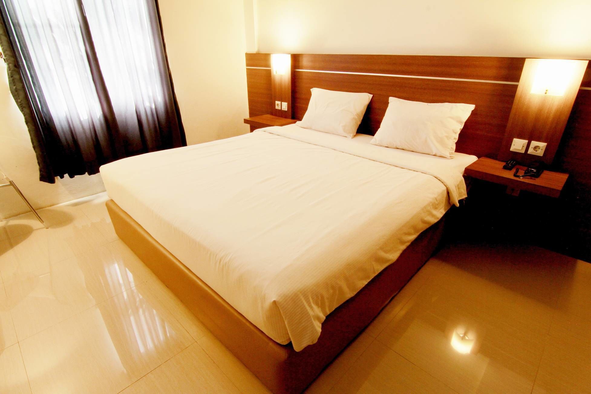 A hotel room with a large bed, two bedside tables, and a nightstand with a lamp.