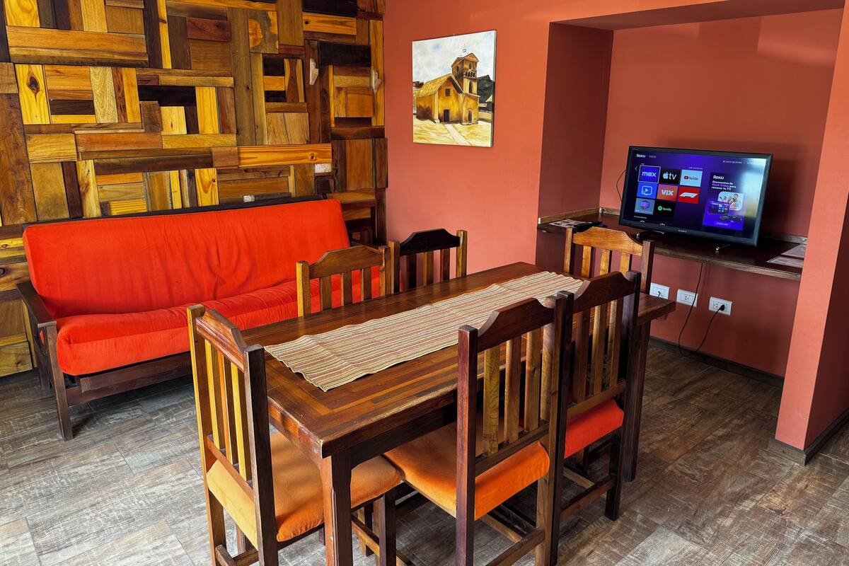 Ein Essbereich mit einem Holztisch, Stühlen, einem roten Sofa und einem Fernseher auf einem Schrank.