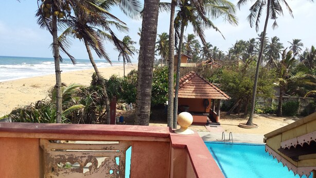 Une vue sur la plage avec une piscine, des palmiers et une petite cabane.