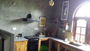 Une cuisine compacte équipée d’une cuisinière, d’un évier et de meubles en bois. Une affiche est visible sur le mur, et une fenêtre laisse entrer la lumière naturelle.