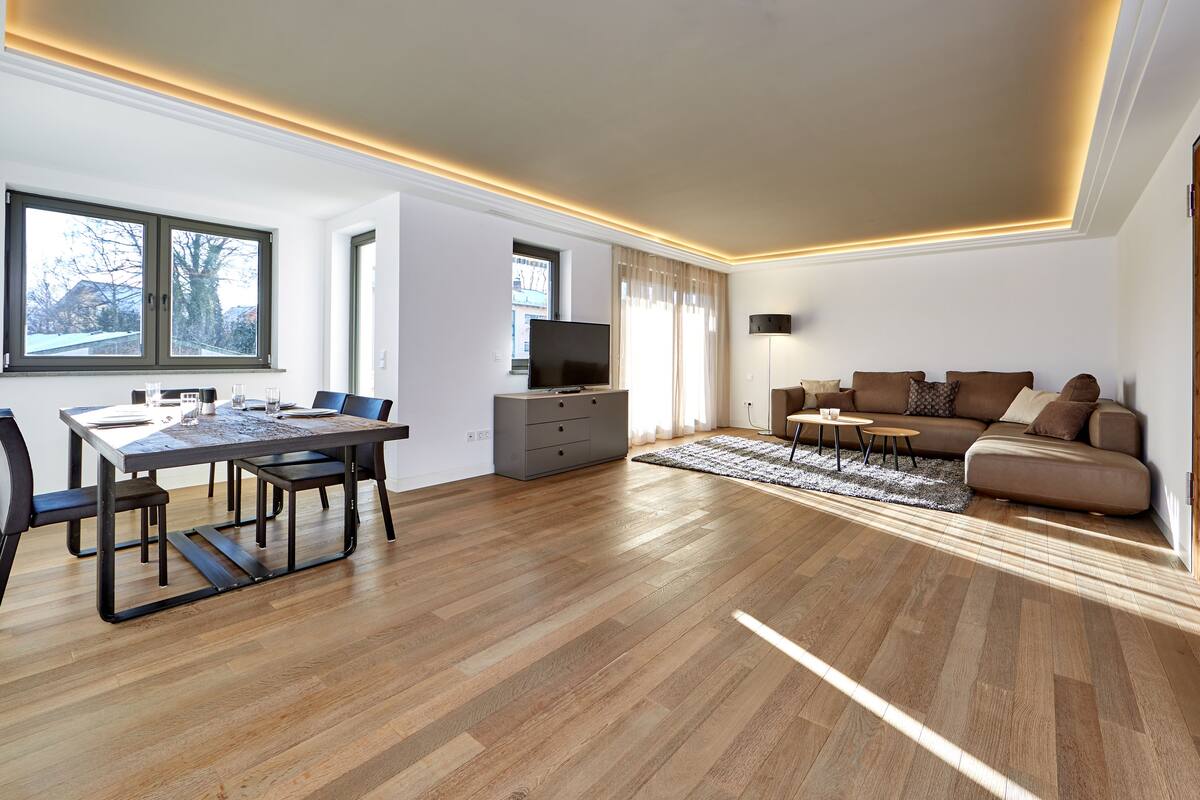Una sala de estar moderna con comedor, piso de madera y un ventanal grande.