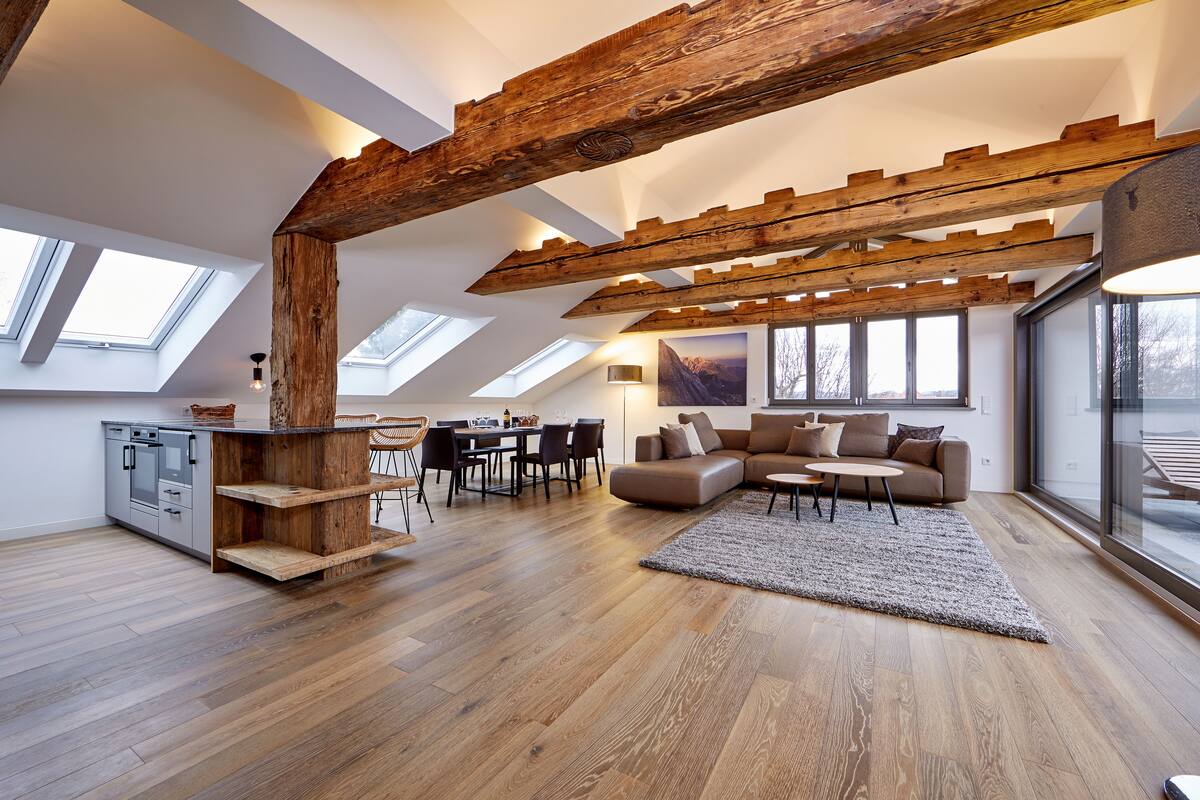 Amplio espacio tipo loft con vigas de madera a la vista, comedor y cocina equipada con electrodomésticos modernos.