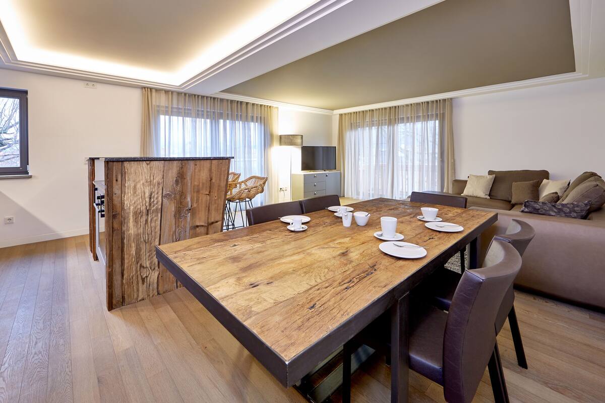 Una sala moderna con una mesa de comedor de madera para cuatro personas, un sofá y un televisor.