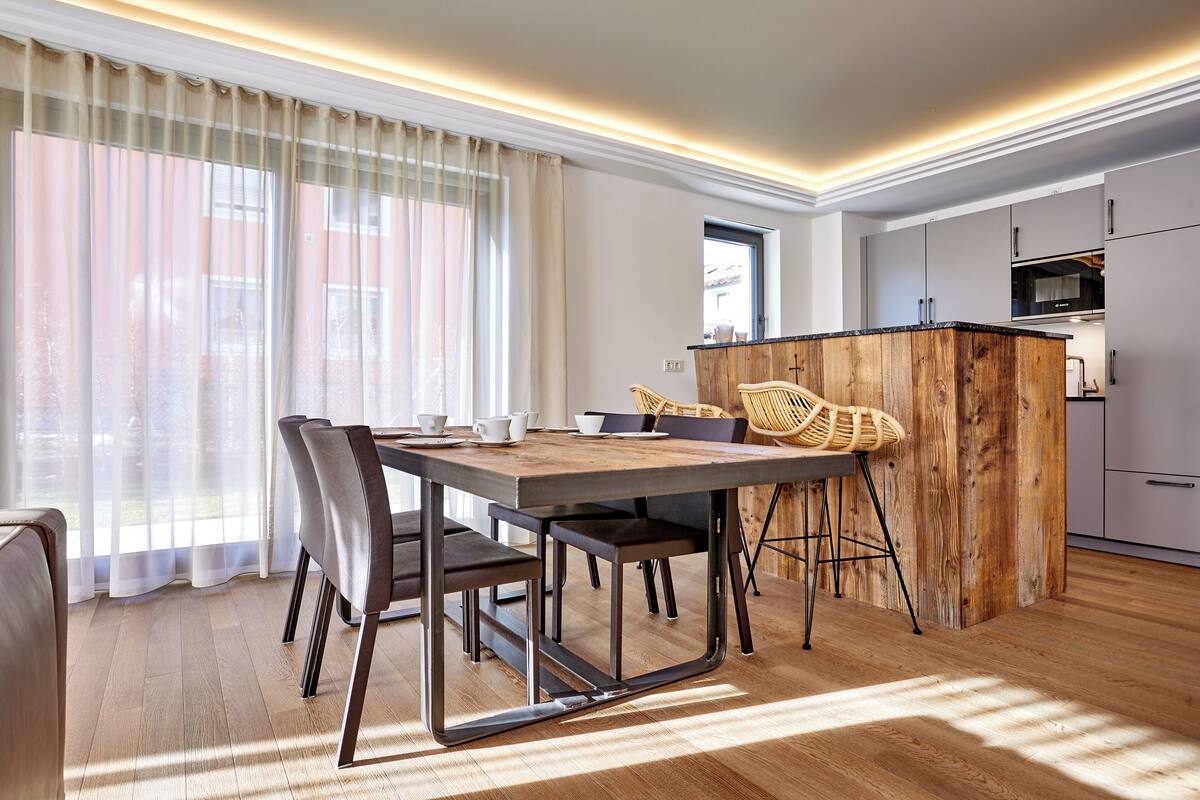 Una cocina moderna con armarios blancos, una isla de madera y un comedor con mesa y sillas.