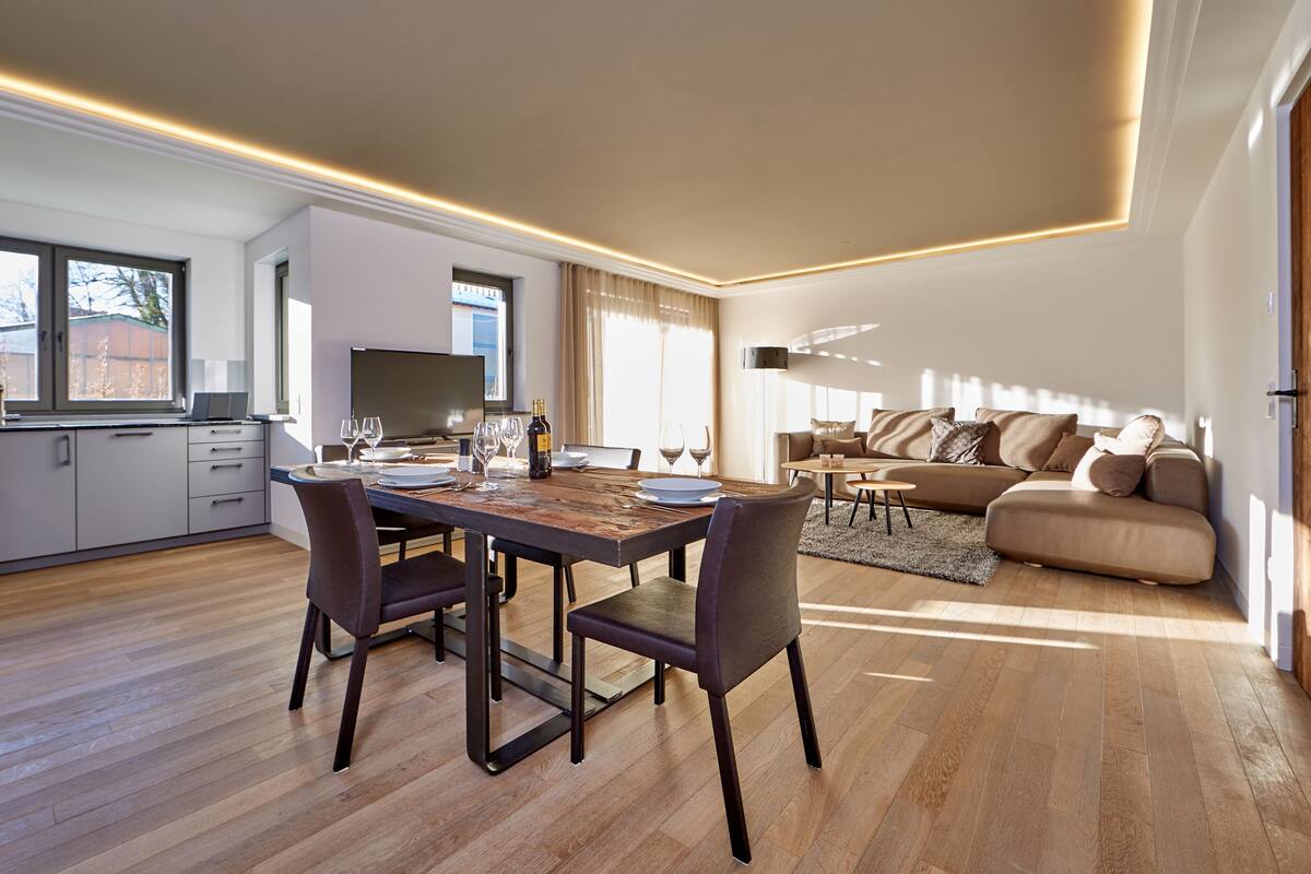 Una sala de estar moderna con comedor, suelo de madera y un ventanal que proporciona luz natural.