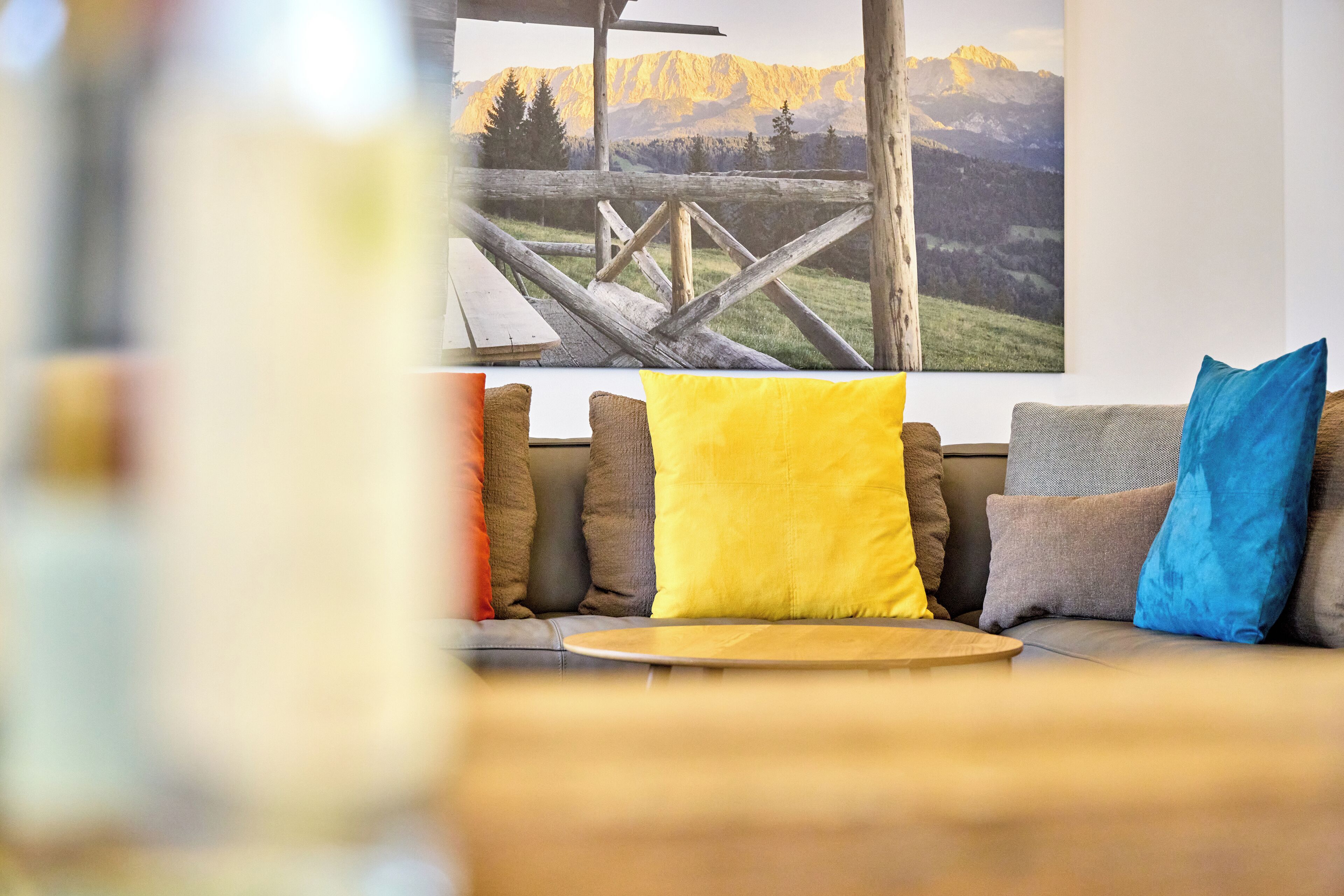 Un área de estar acogedora con una mesa de madera, un sofá con cojines de colores y un cuadro grande de un paisaje montañoso en la pared.