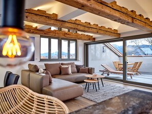 Una sala moderna con sofá, una silla de mimbre y una mesa de comedor. Amplias ventanas ofrecen vistas al exterior.