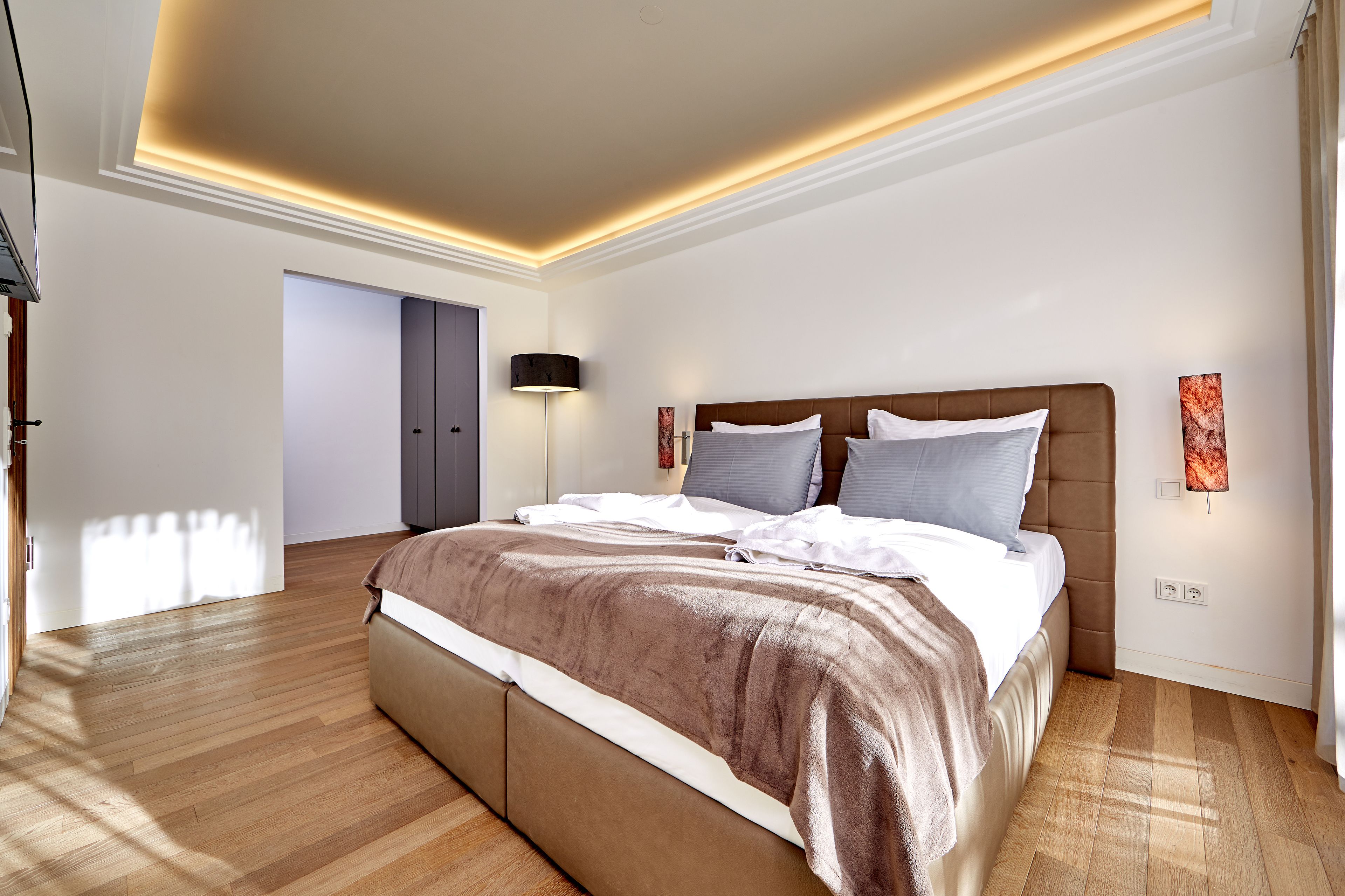 Une chambre à coucher moderne avec un grand lit, un plancher en bois et un éclairage encastré au plafond.