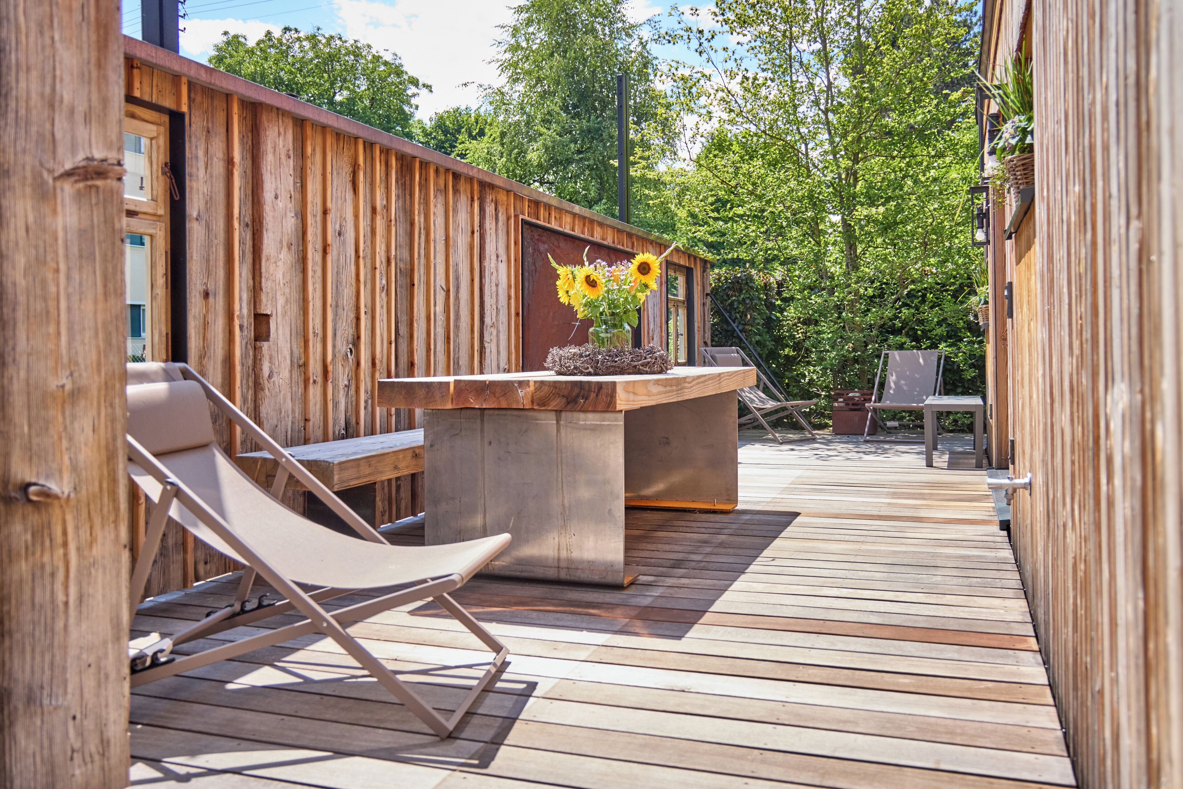 A wooden deck with a concrete table and chairs, a wooden fence, and a view of trees.