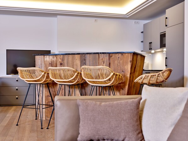 Una cocina moderna con una isla de madera, cuatro sillas de mimbre, un televisor de pantalla plana y un sofá con un cojín.