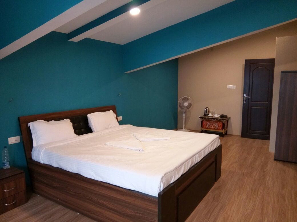 Una camera da letto con un letto in legno, pareti color verde acqua, pavimento in legno, un comodino, una ventola e una porta.