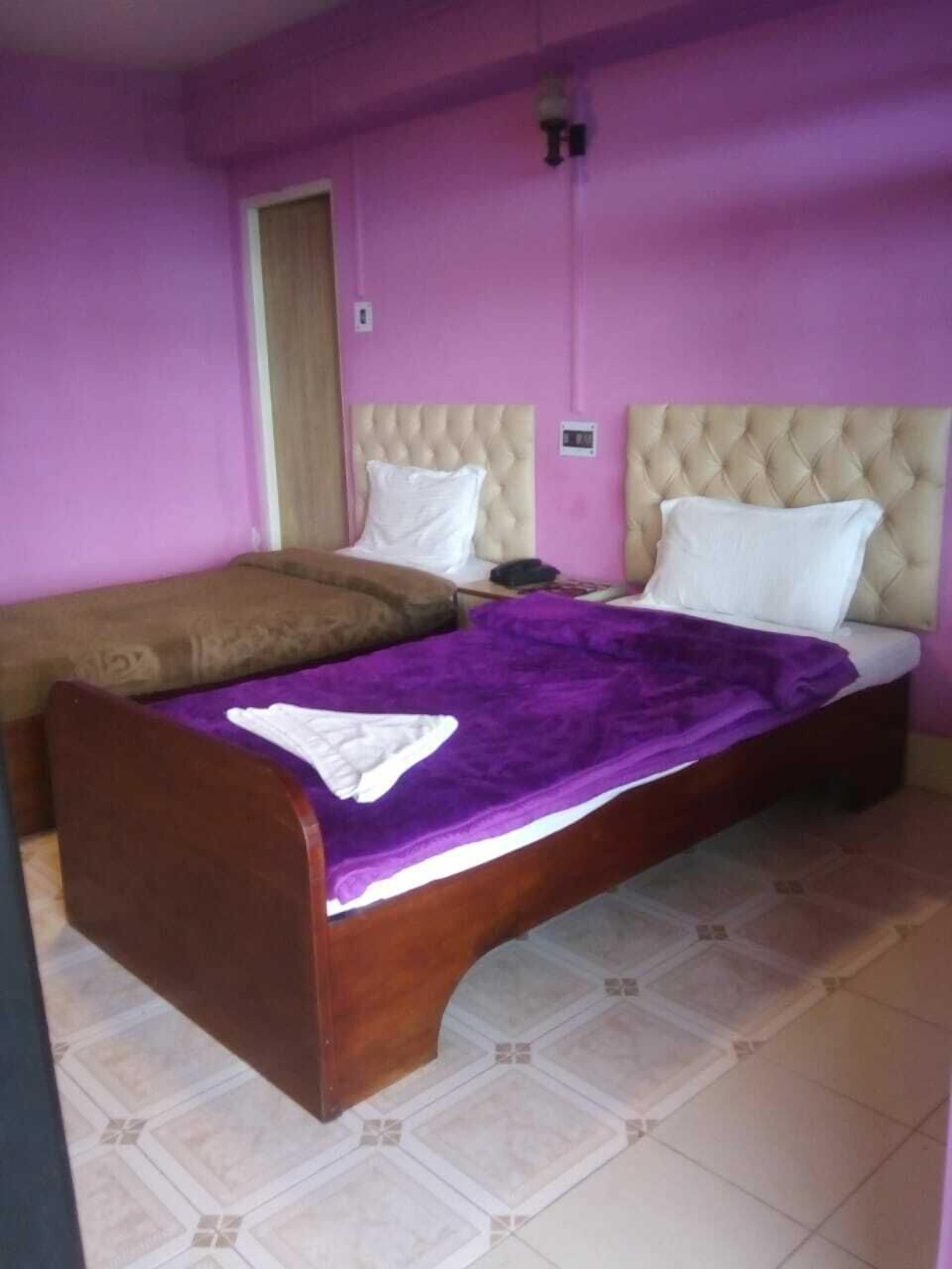 Un dormitorio con dos camas, una con una manta púrpura y la otra con una manta marrón.
