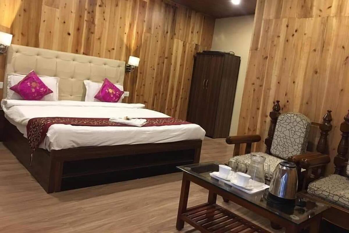A wooden-paneled room with a bed, a table with a kettle, and a chair.