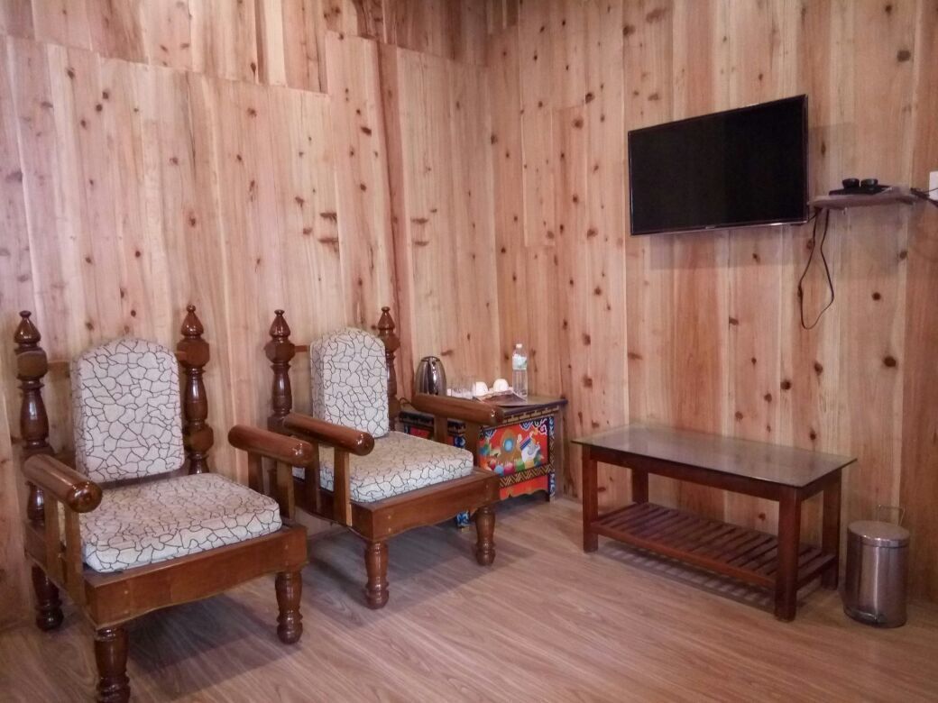 A room with wooden paneled walls, two upholstered chairs with a cracked pattern, a wooden table, a television mounted on the wall, and a small side table with decorative items.
