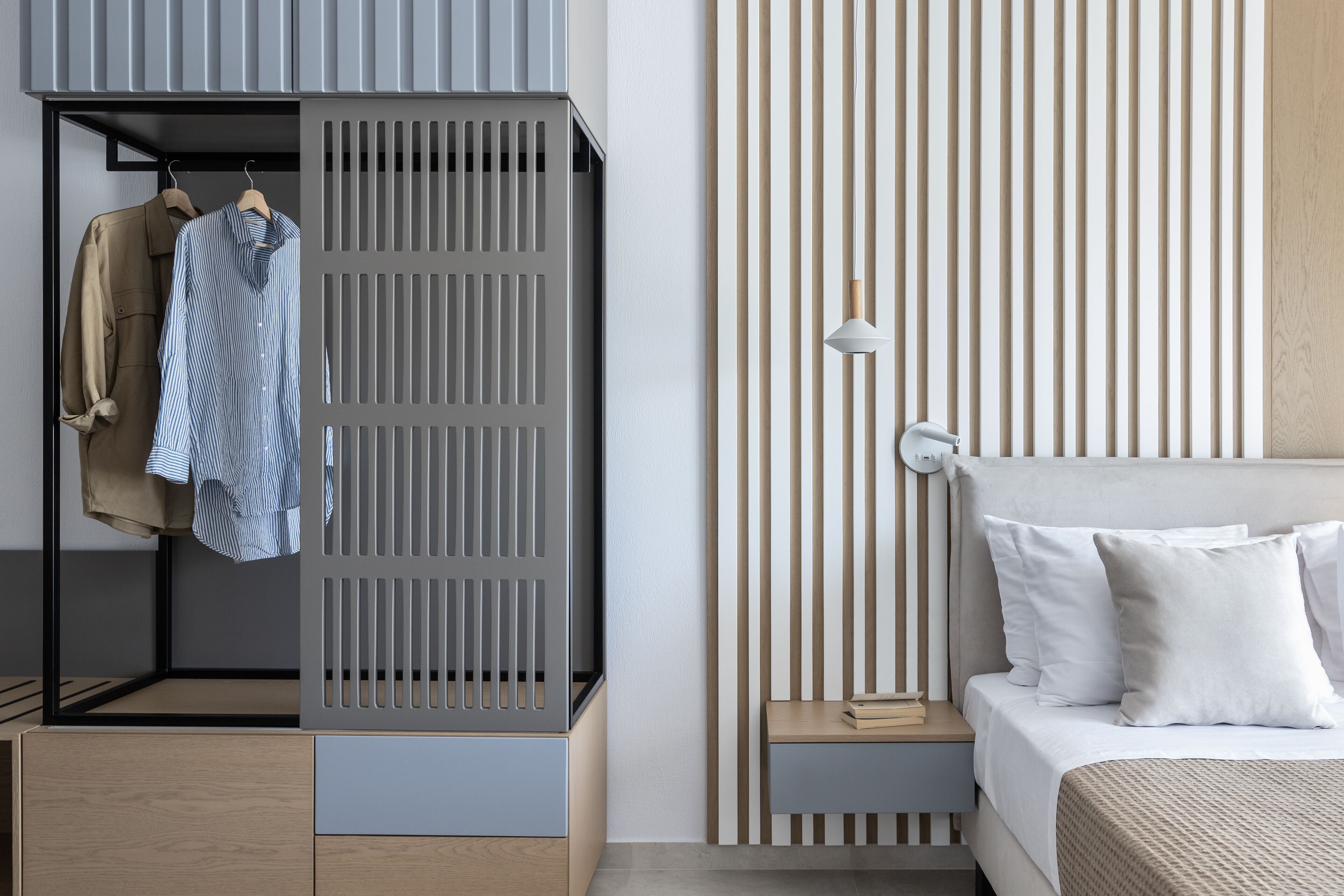 A modern bedroom with a bed, bedside table, and a wardrobe with hanging clothes.