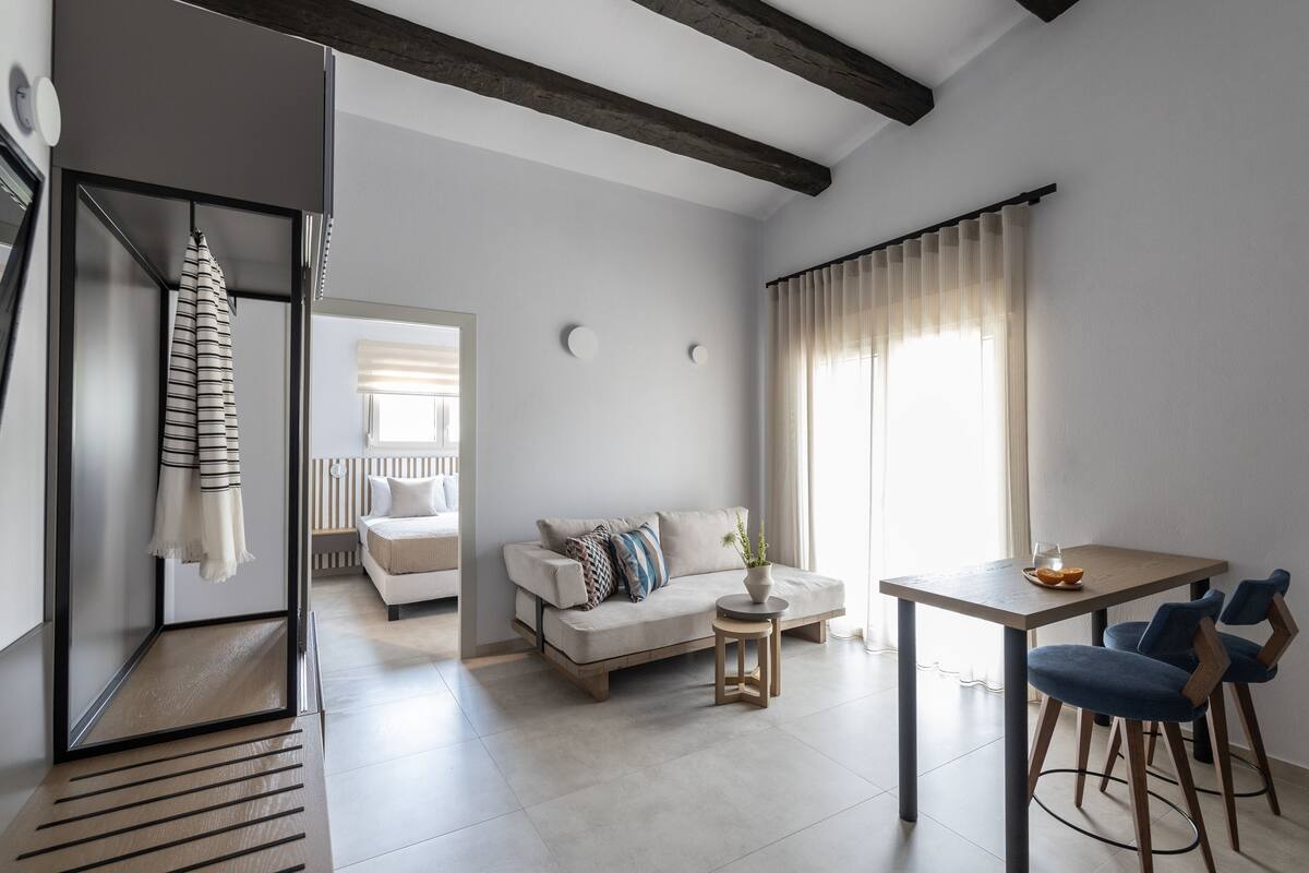 A modern living room with a sofa, a dining table with chairs, a small side table, and a window with curtains.