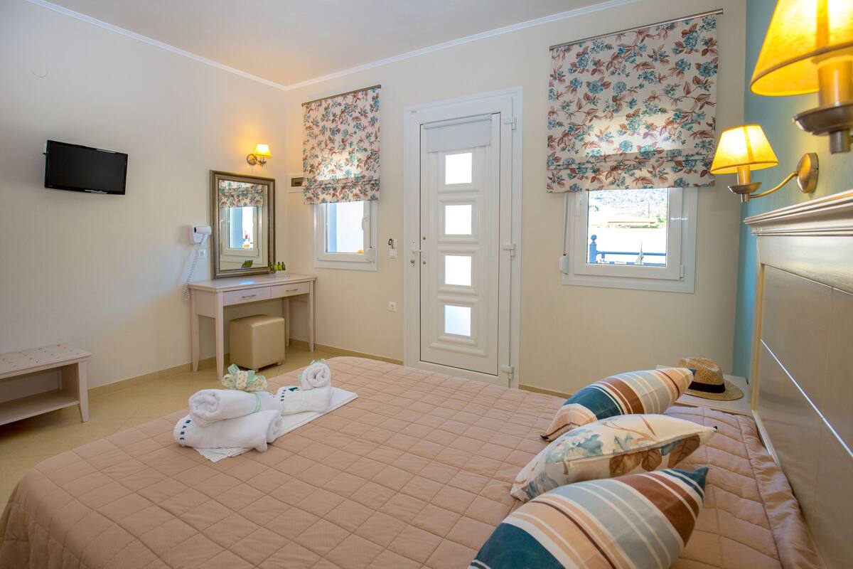 A hotel room with a bed, a desk, a mirror, a television, and a window with floral curtains.