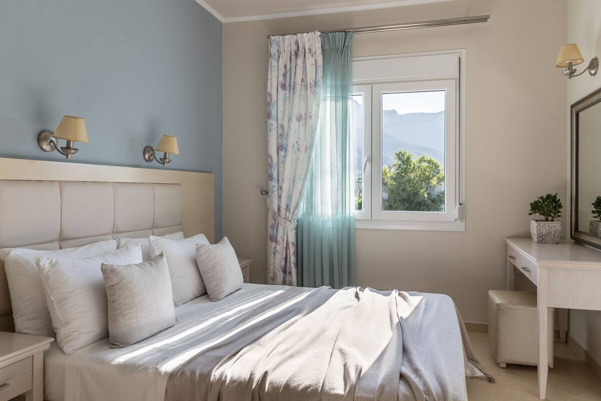 A bedroom with a bed, nightstands, a desk, a mirror, and a window with curtains.