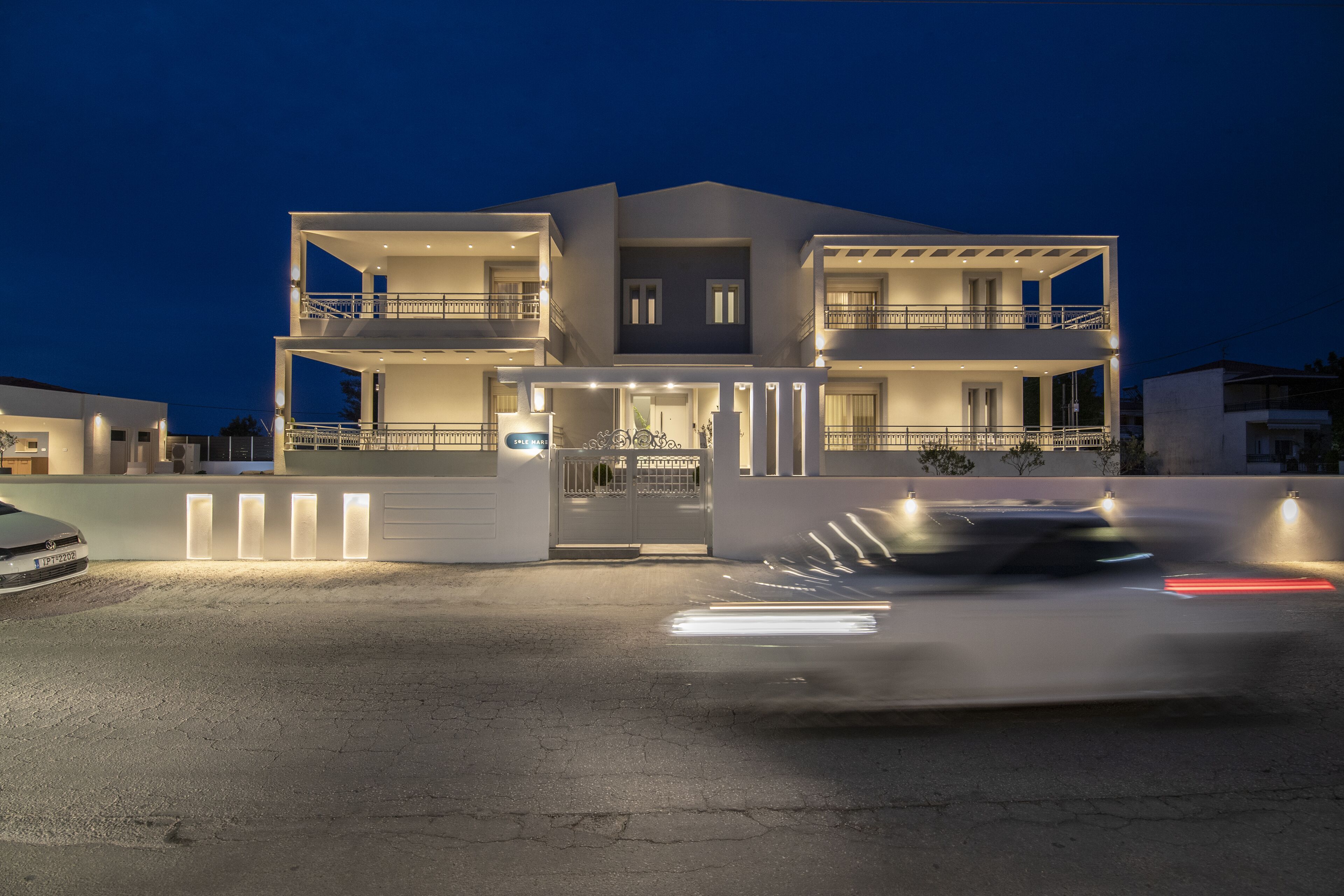 A modern two-story house with a gated entrance, multiple balconies, and a driveway.