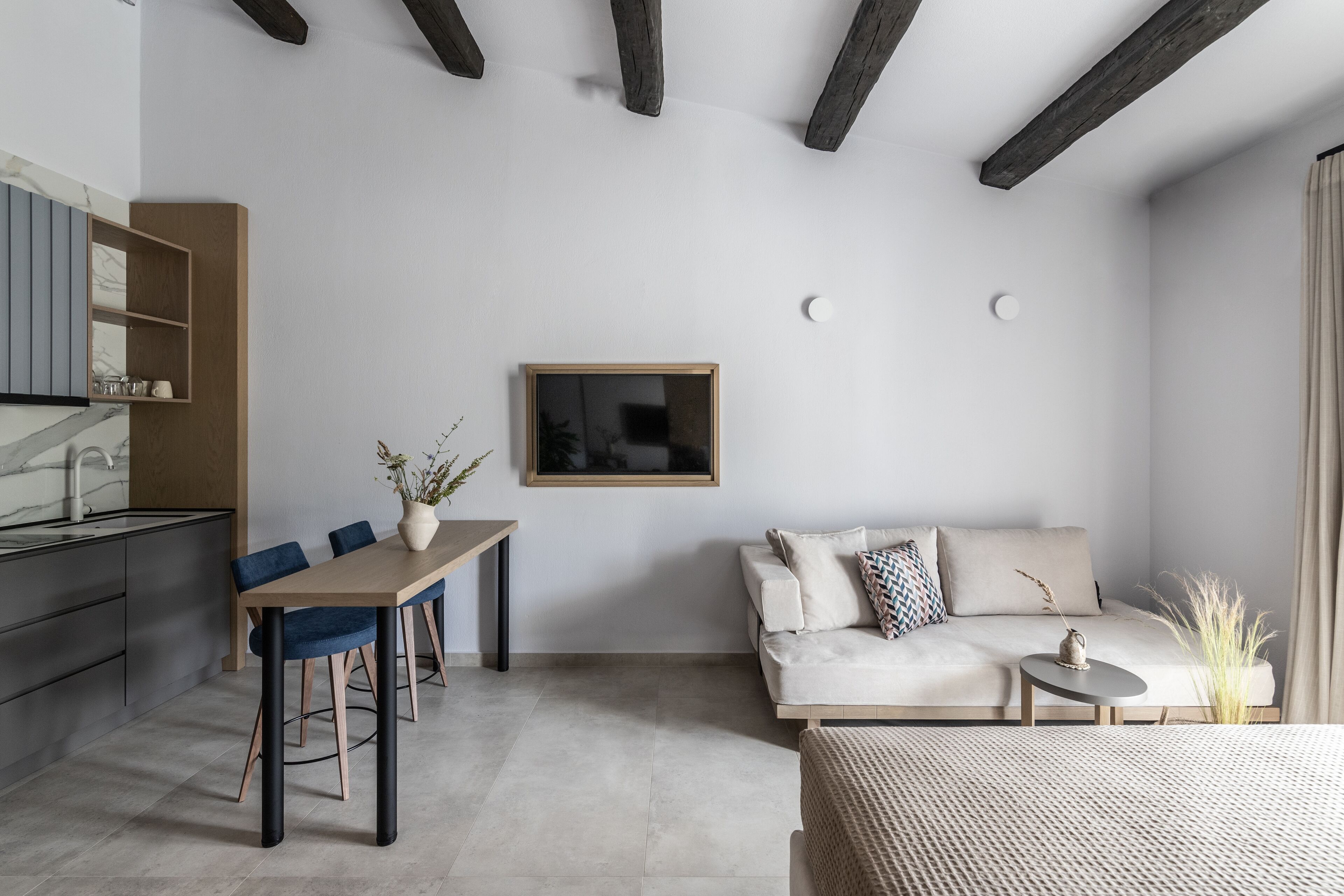 A modern living room with a sofa, a dining table with chairs, and a kitchen area with cabinets and a countertop.
