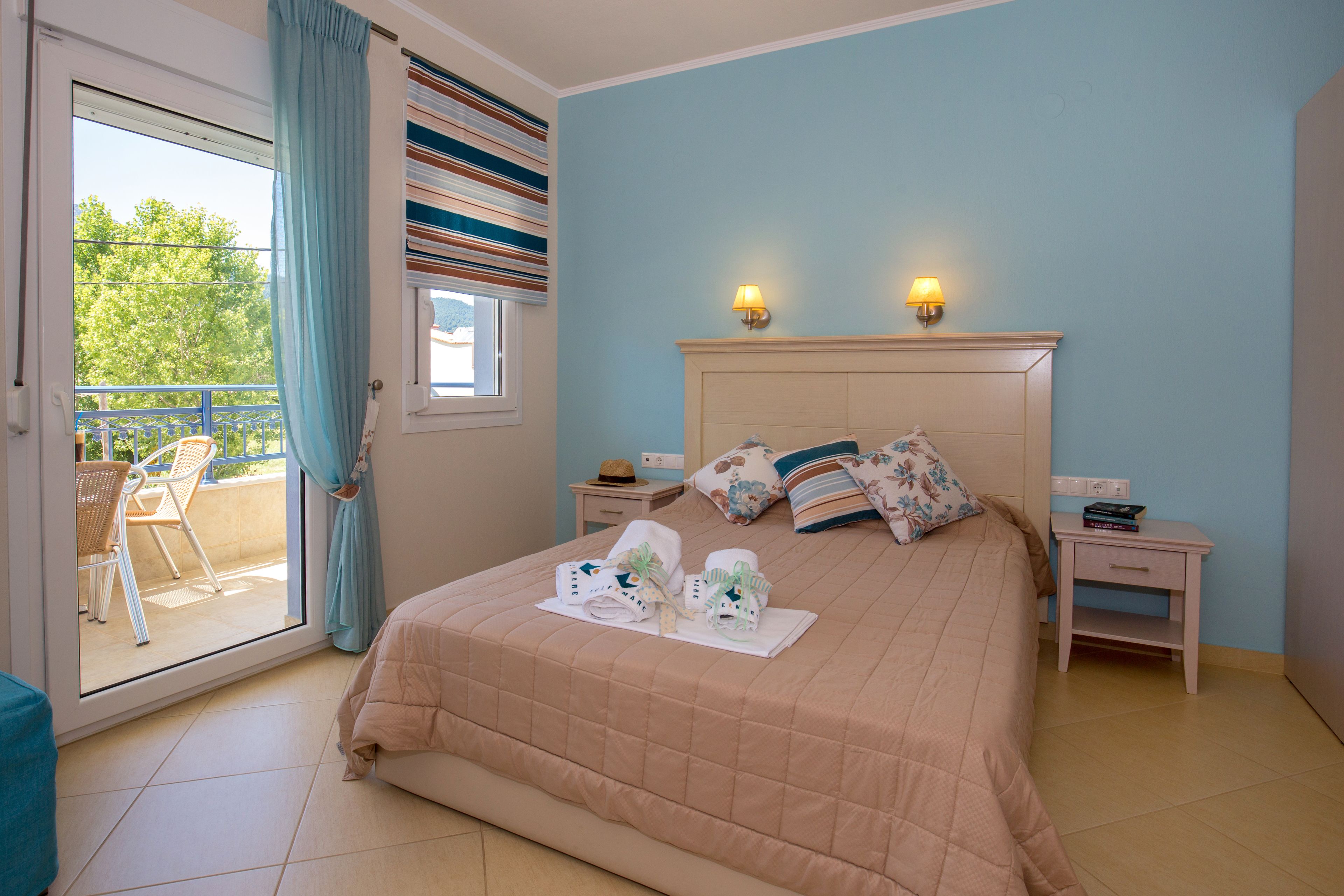 A bedroom with a bed, two bedside tables, a nightstand, a window with curtains, and a view of the outdoors.
