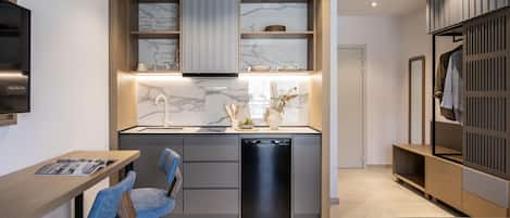 A modern kitchen with a built-in stove, a dishwasher, and a marble backsplash. There is a dining area with a table and chairs, and a wardrobe with a mirror.