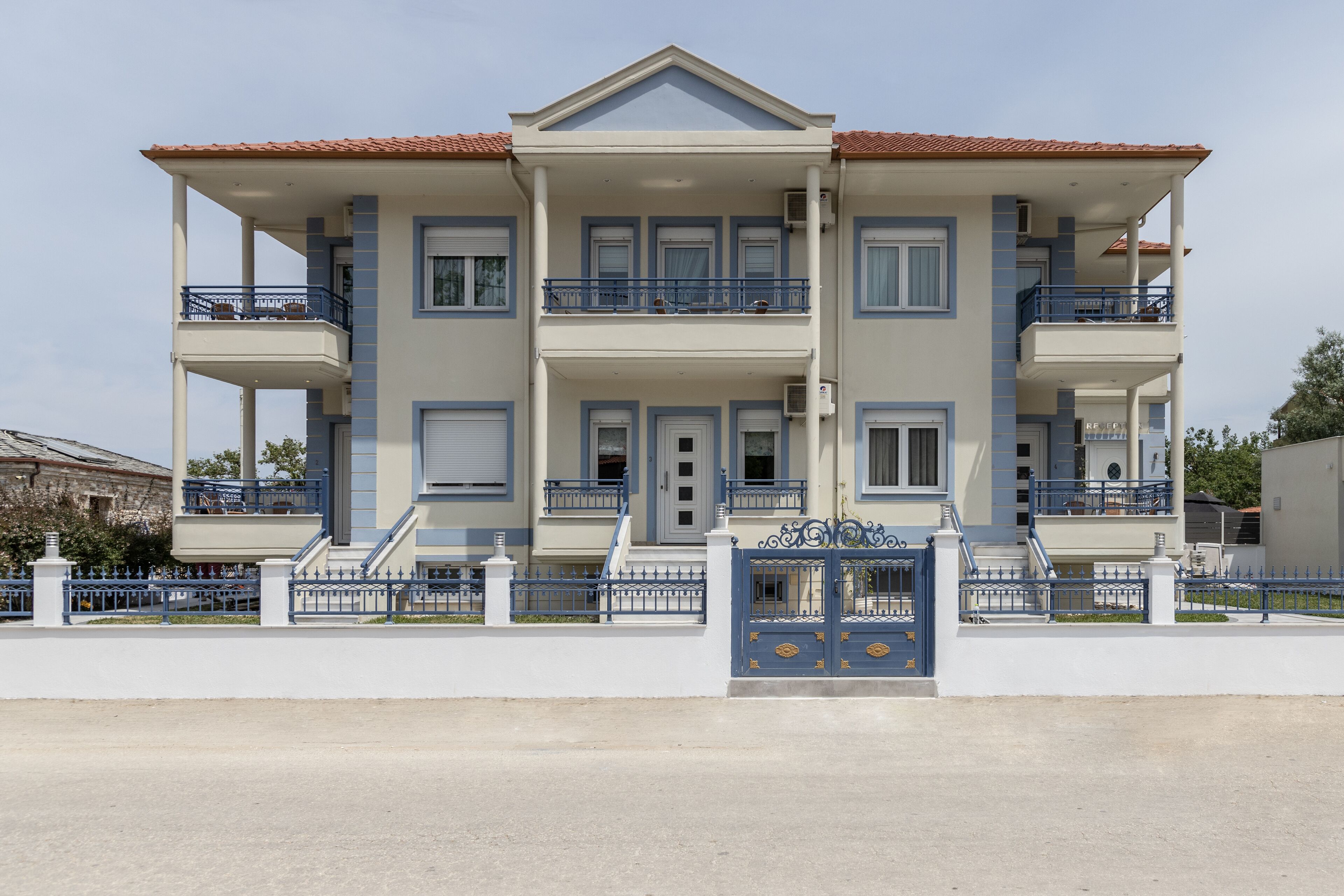 A two-story building with balconies, a gated entrance, and a clear sky.