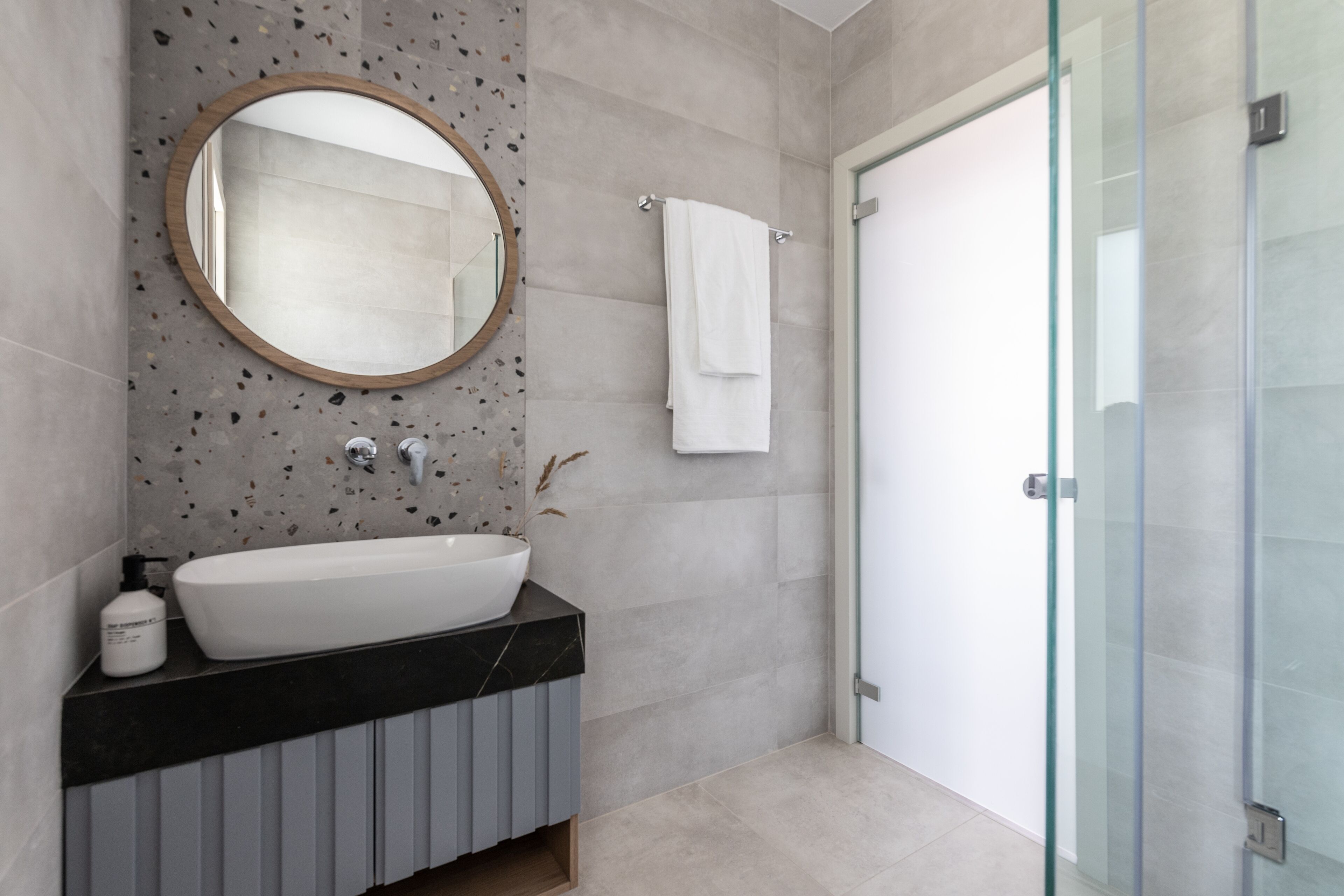 A modern bathroom with a freestanding bathtub, a round mirror, and a glass shower enclosure.