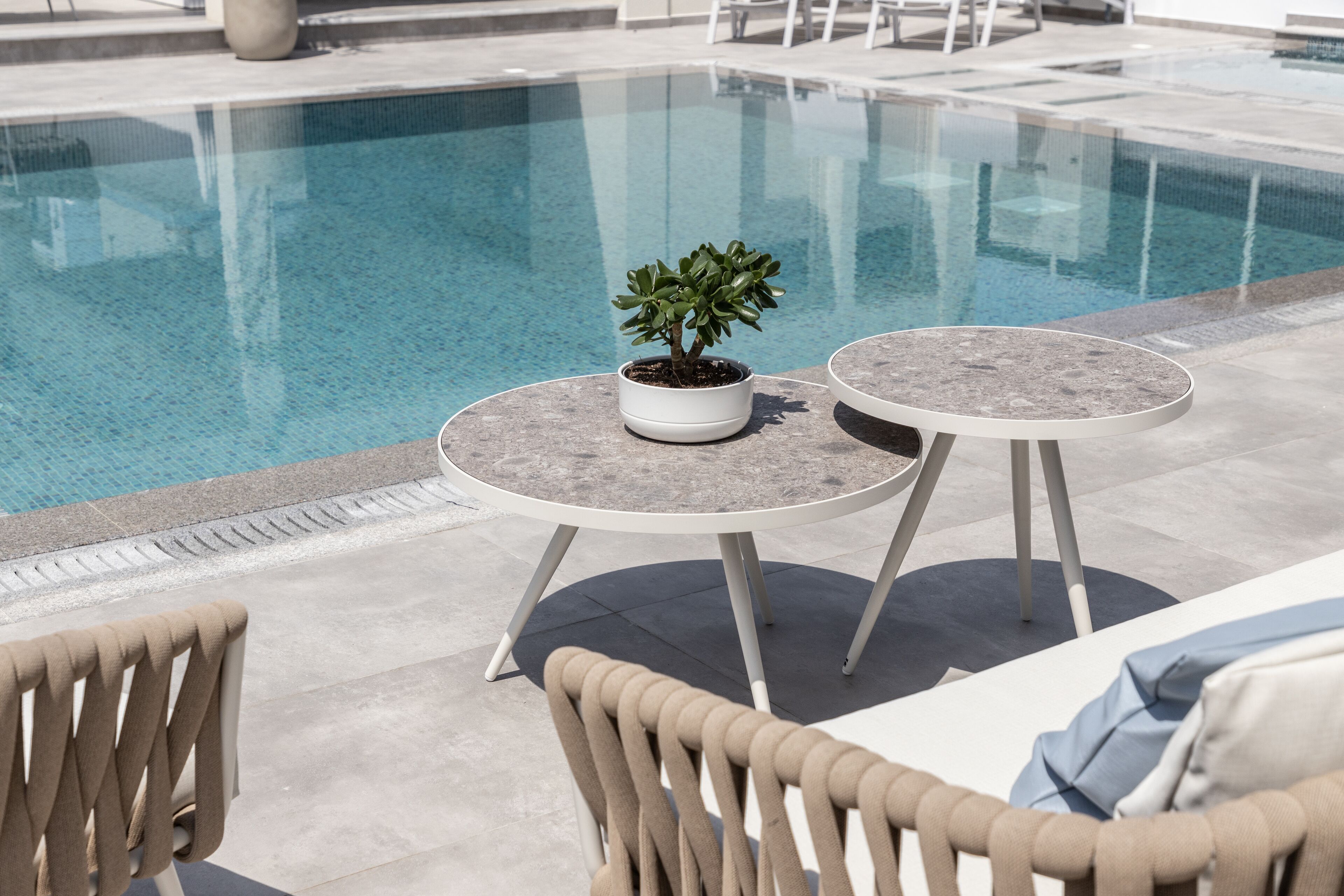 A poolside area with two round tables, a potted plant, and lounge chairs.