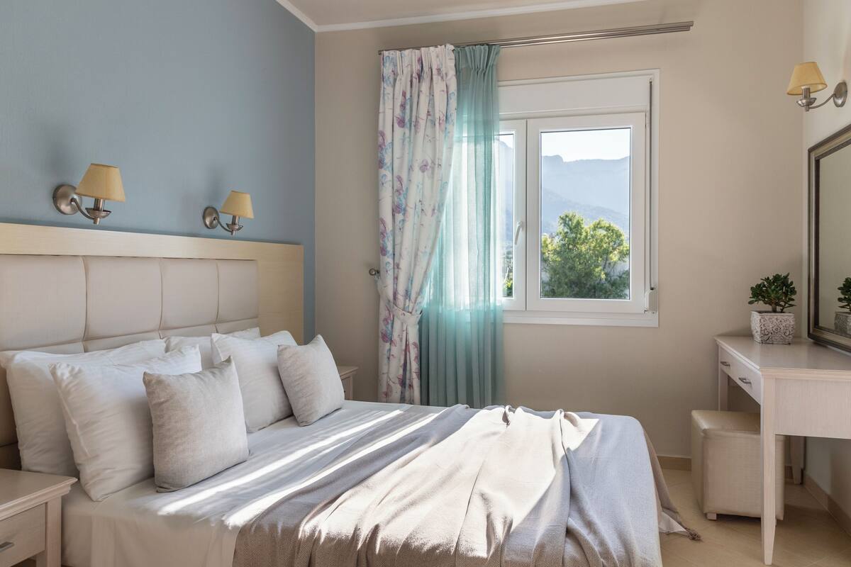 A bedroom with a bed, nightstands, a desk, a mirror, and a window with curtains.