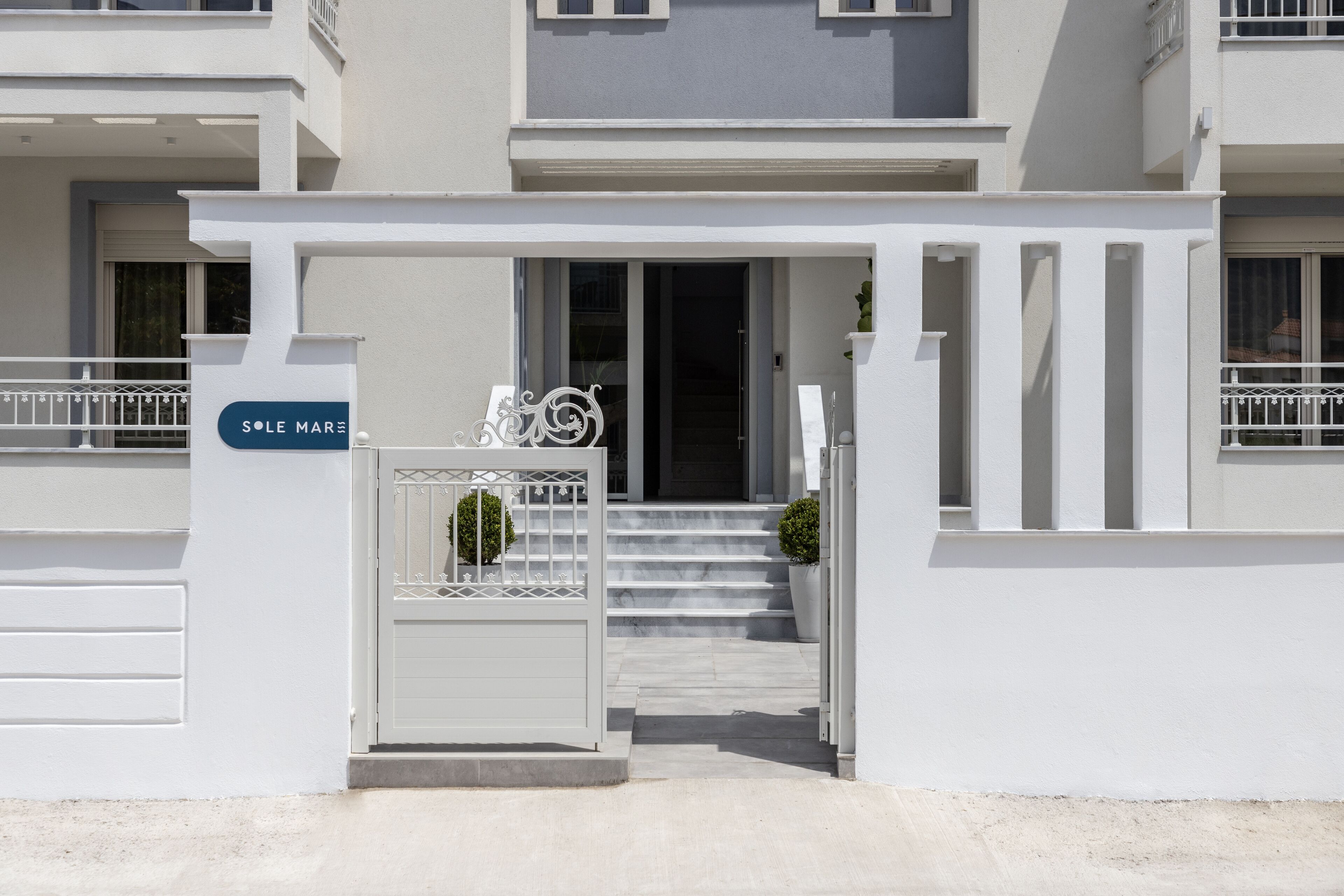 Un edificio moderno con fachada blanca, entrada protegida por una reja y una escalera que lleva a la entrada.