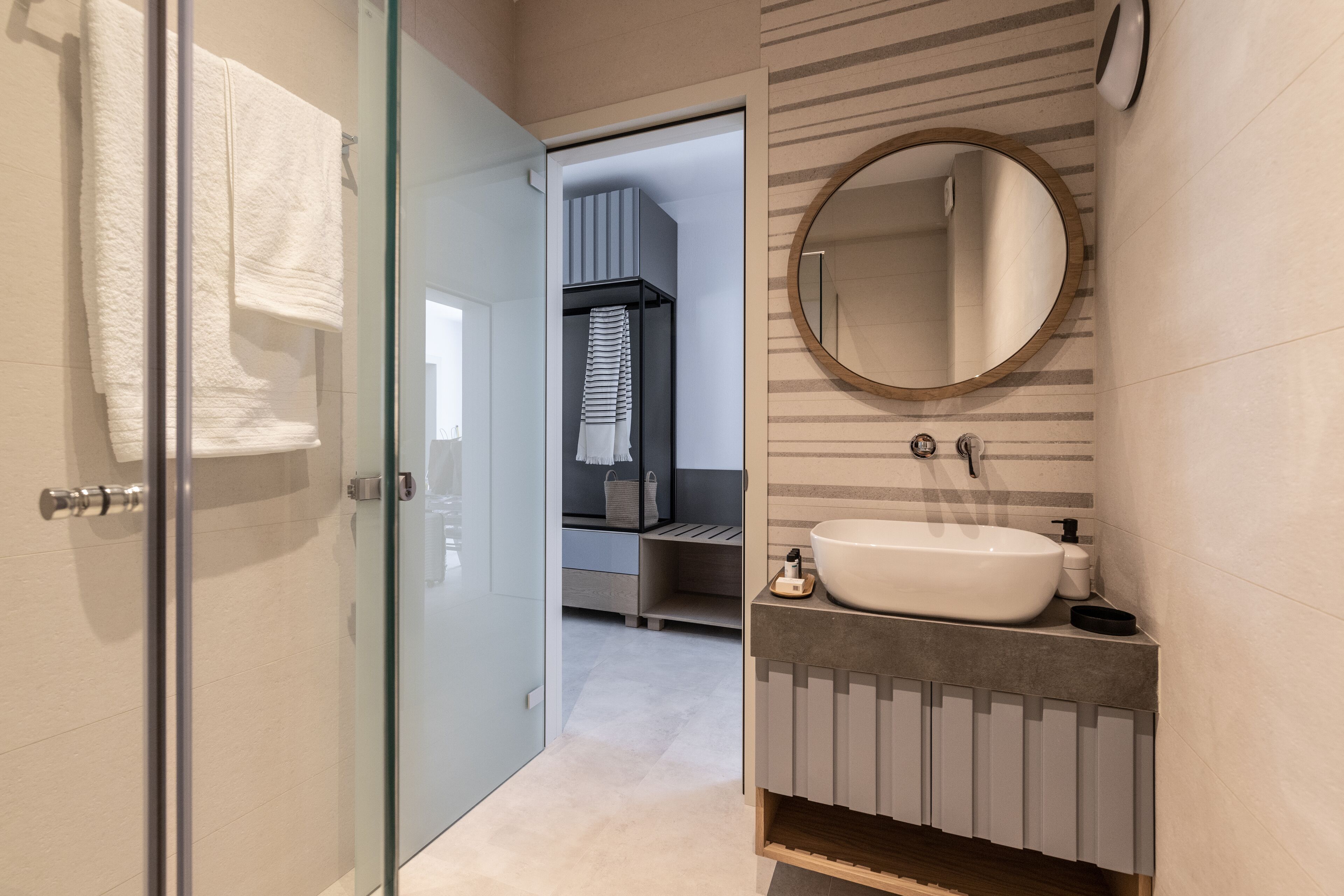 A modern bathroom with a glass shower door, a white sink, and a round mirror.