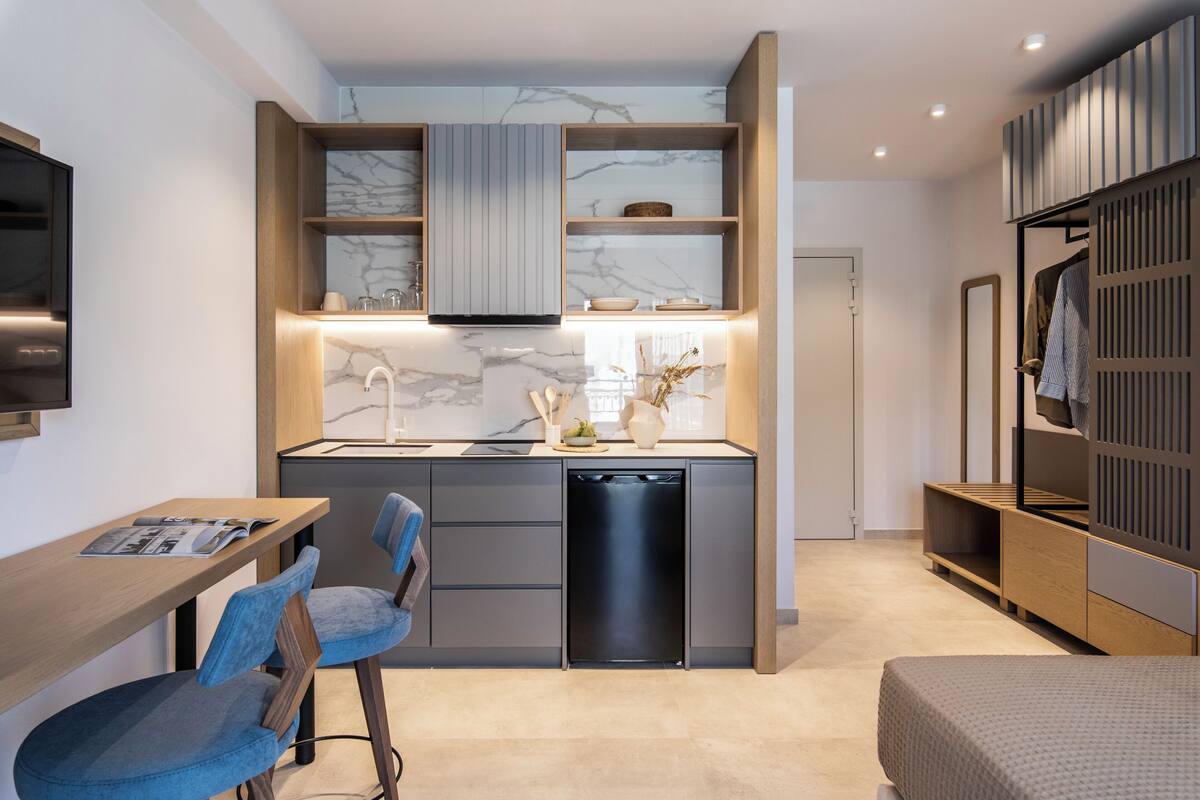 A modern kitchen with a built-in stove, a dishwasher, and a marble backsplash. There is a dining area with a table and chairs, and a wardrobe with a mirror.