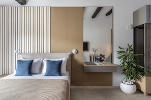 A modern hotel room with a bed, bedside table, a potted plant, and a mirror reflecting the room.