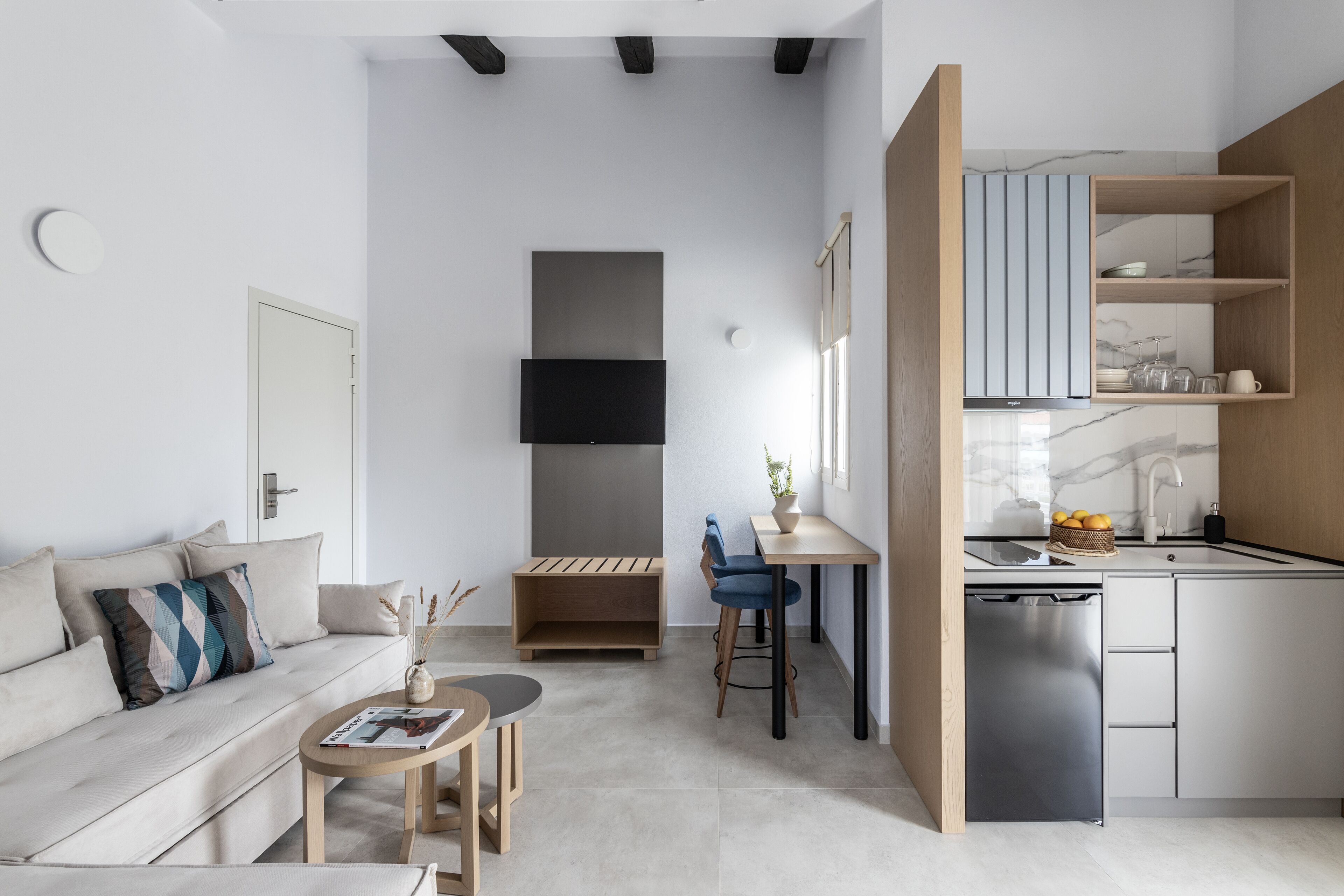 A compact living space with a sofa, a small dining table, a kitchen area with a dishwasher, and a TV mounted on the wall.