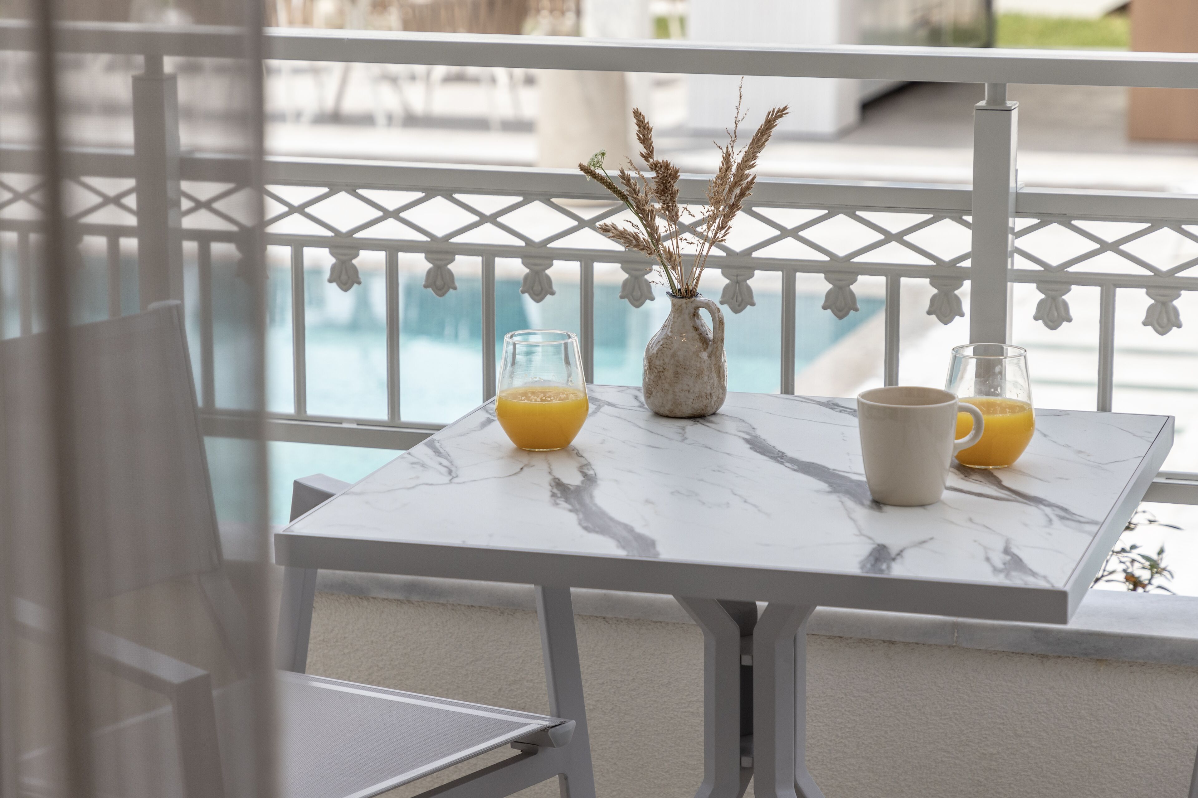 A balcony with a marble table, two glasses of orange juice, and a vase with dried plants.