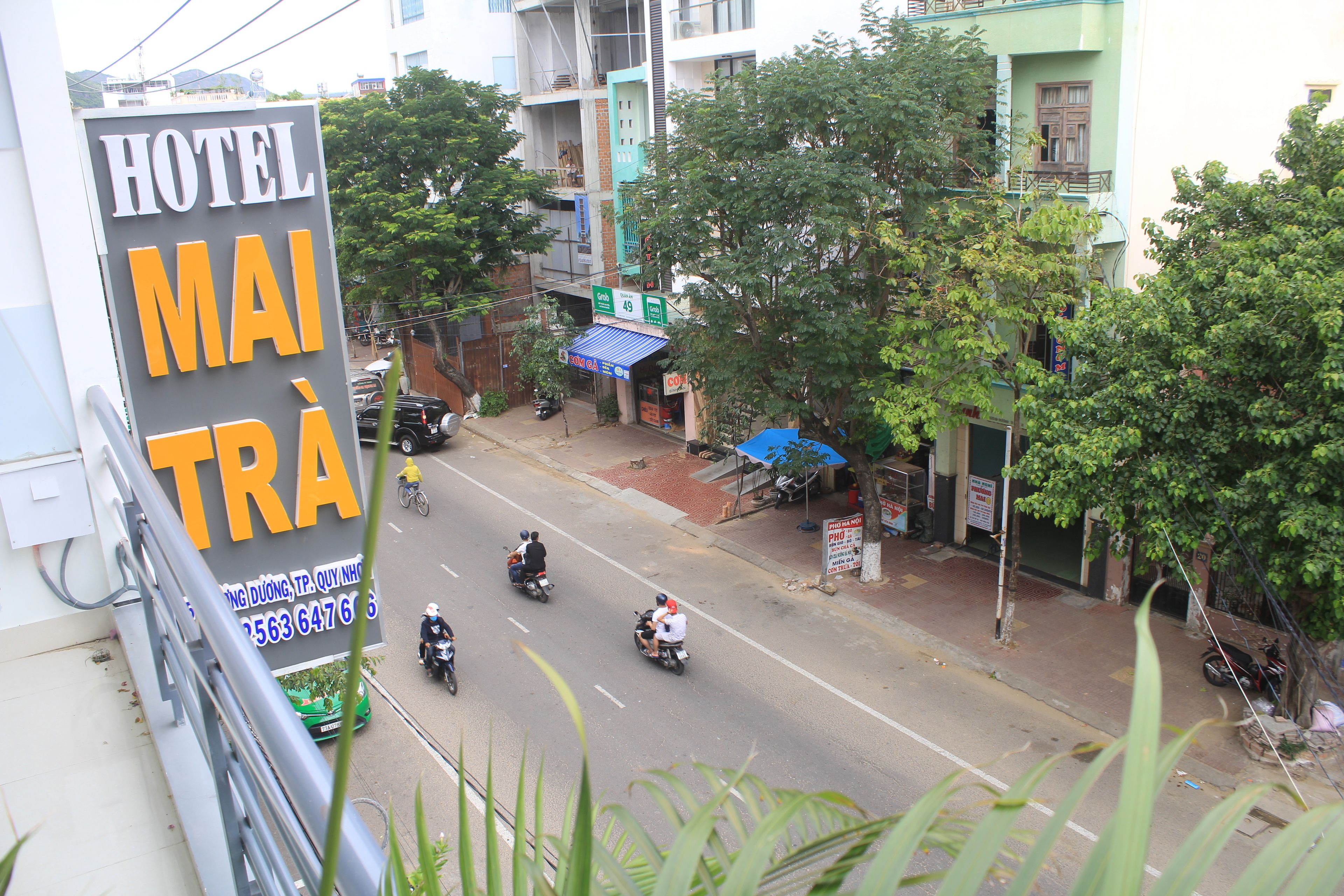A street view with a hotel sign, a blue awning, and a tree-lined sidewalk.