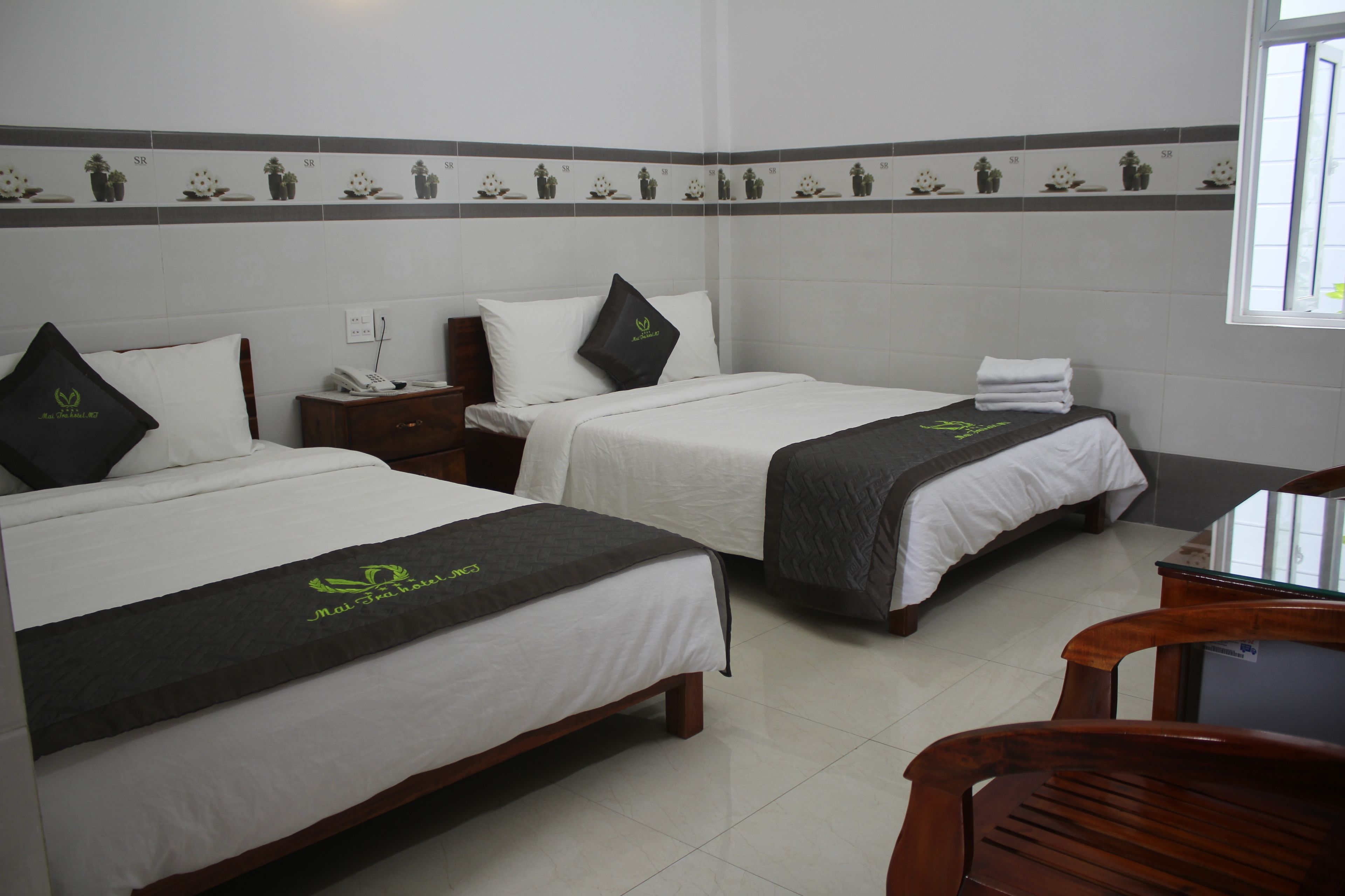 Habitación de hotel con dos camas, cada una con cubrecama blanco y manta gris oscura, y una mesita de noche de madera entre ellas.