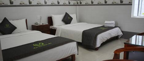 Habitación de hotel con dos camas, cada una con cubrecama blanco y manta gris oscura, y una mesita de noche de madera entre ellas.