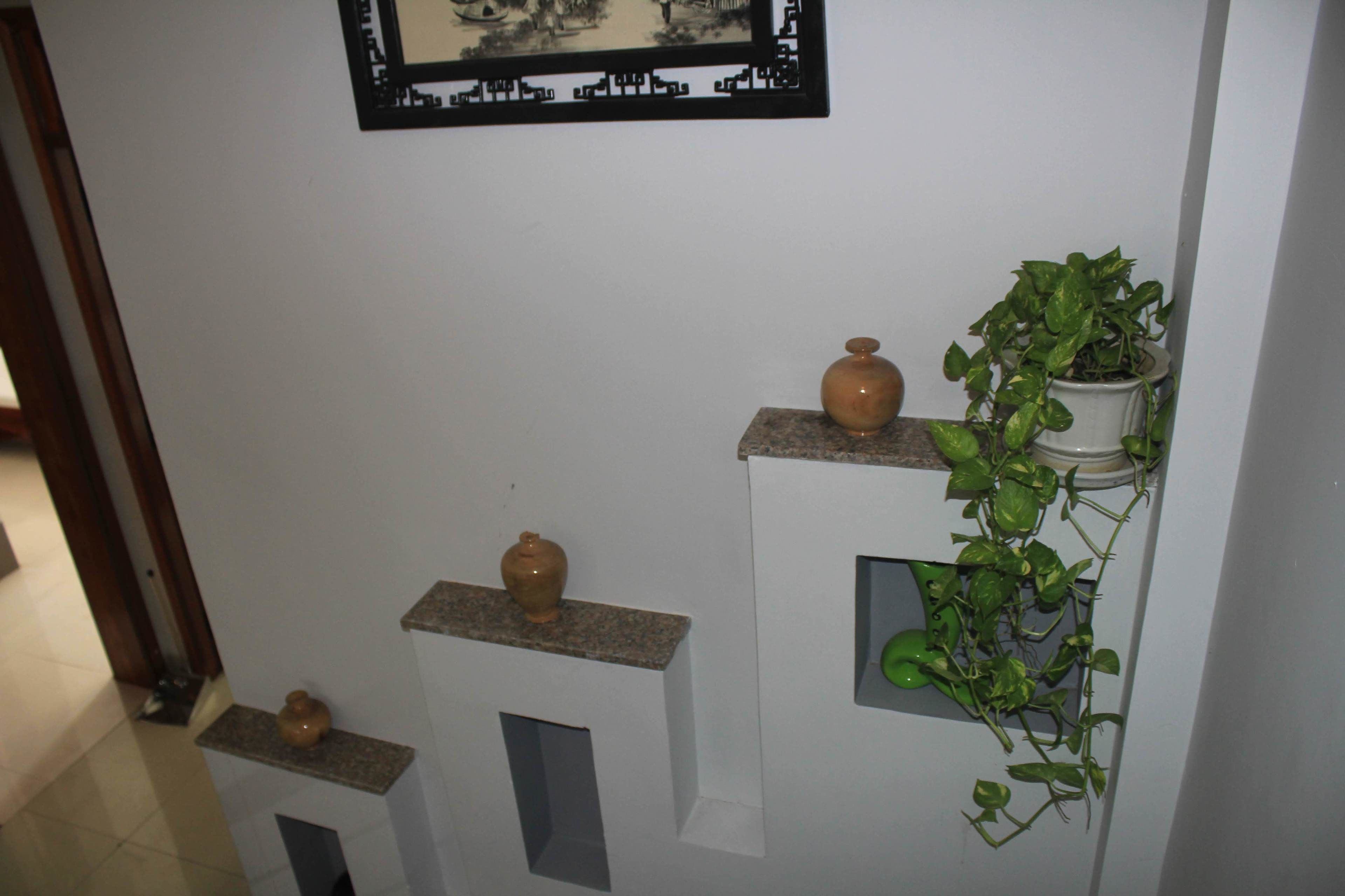 A hallway with shelves holding vases and a potted plant.