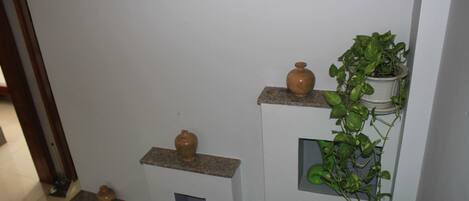 A hallway with shelves holding vases and a potted plant.