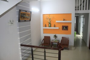 Una escalera con barandilla de madera que lleva a un rellano. En el rellano hay dos sillas de madera y una pequeña mesa con una planta en maceta.